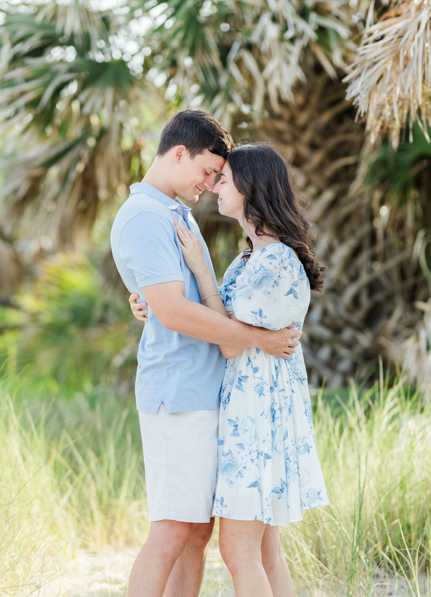 A romantic couple in light blue outfits sharing tender moments together in a natural outdoor setting.