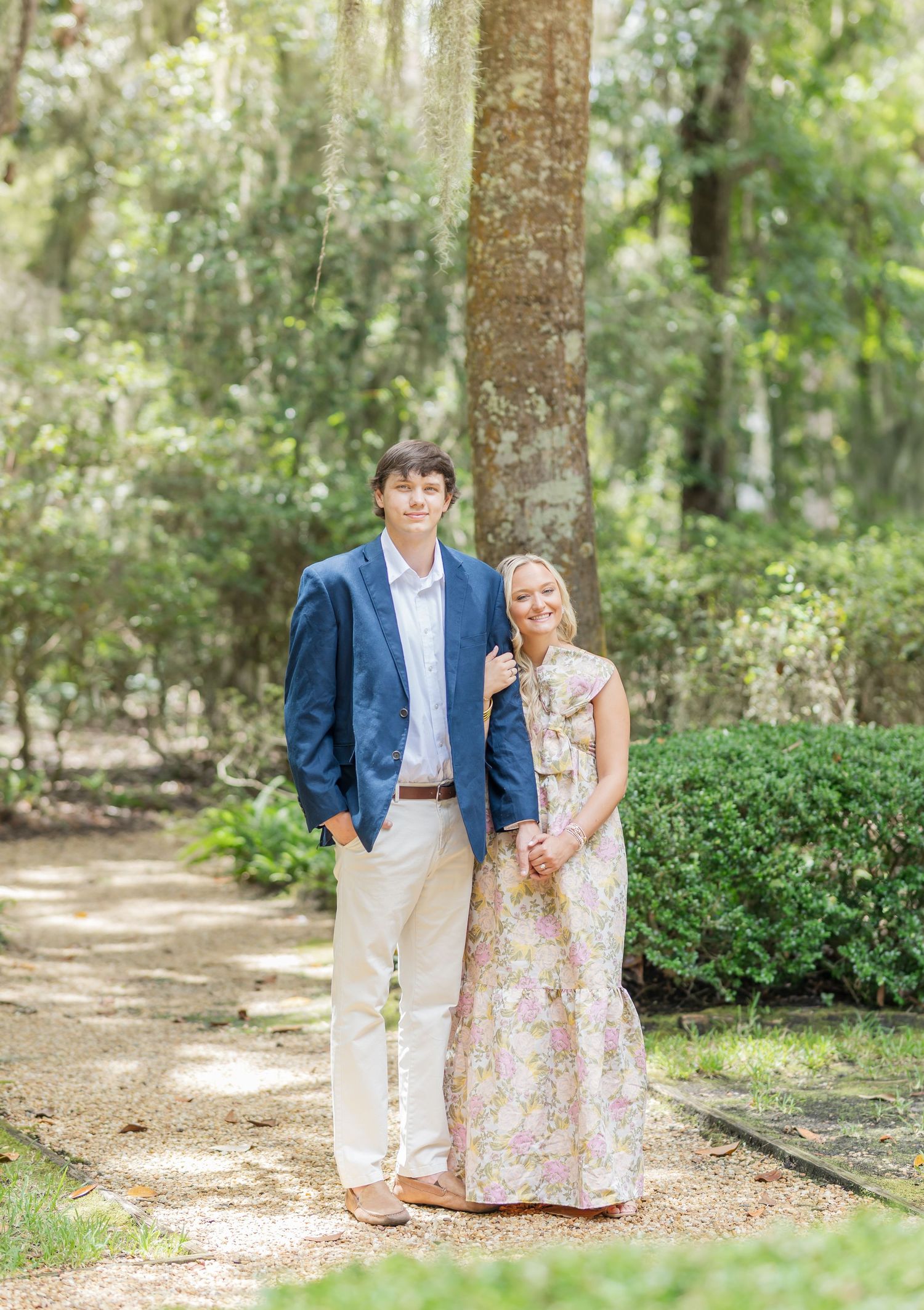 Couple shares intimate moment on tree-lined pathway with Spanish moss hanging overhead.