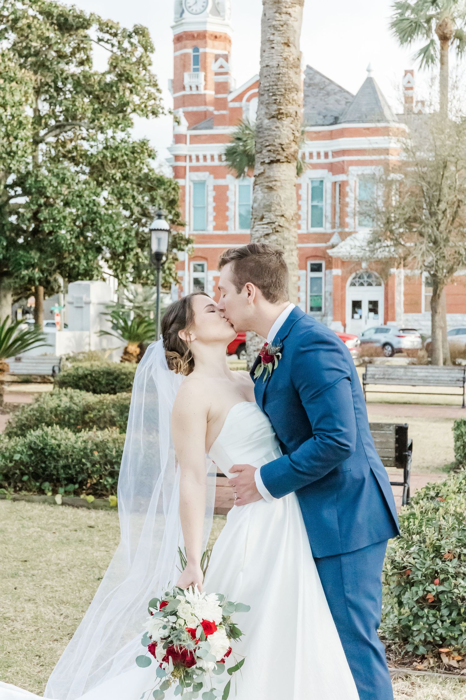 Wedding couple shares romantic moment in garden setting with historic building backdrop.