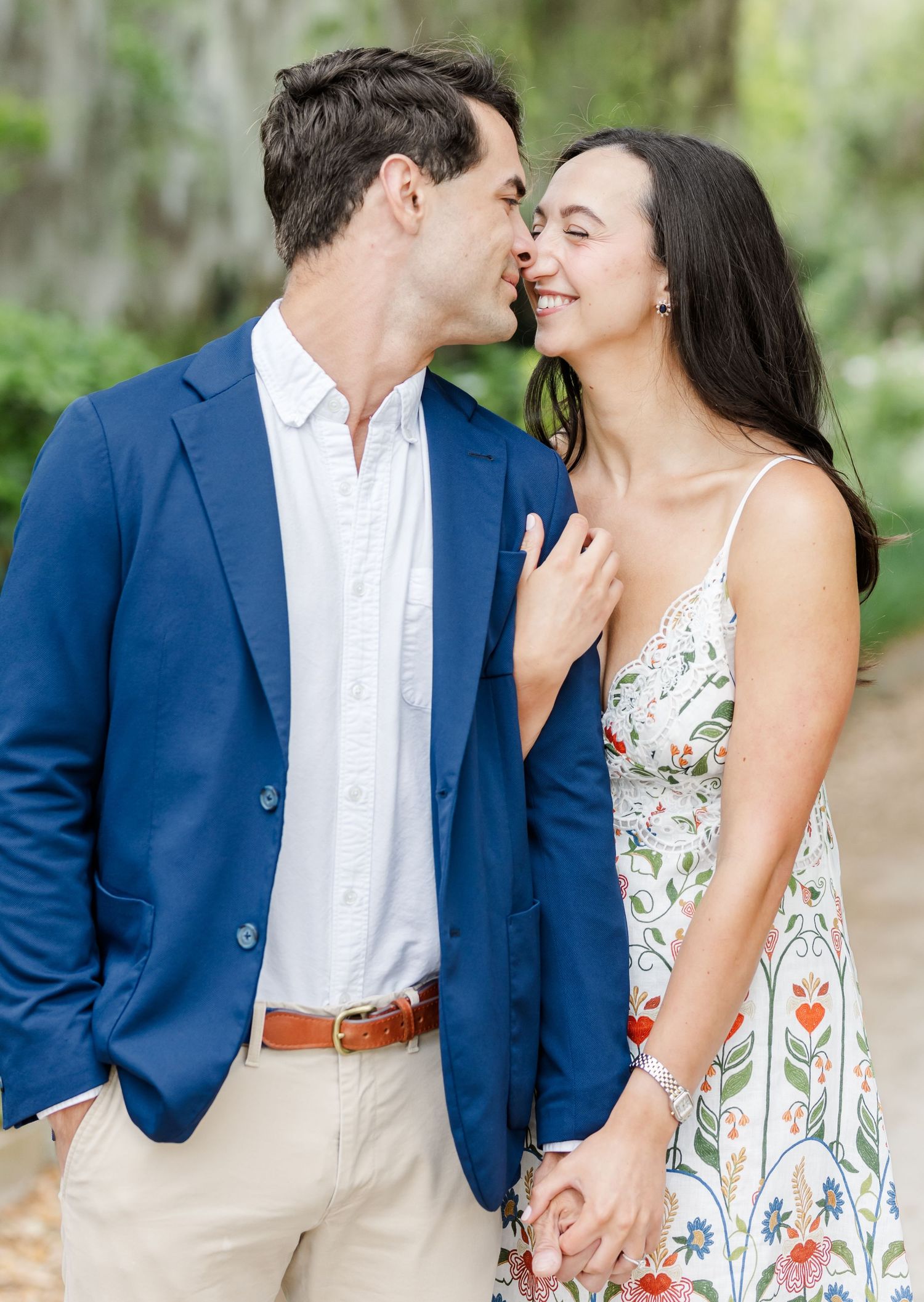 Couple sharing a romantic moment, man in blue blazer and woman in floral dress holding hands outdoors.