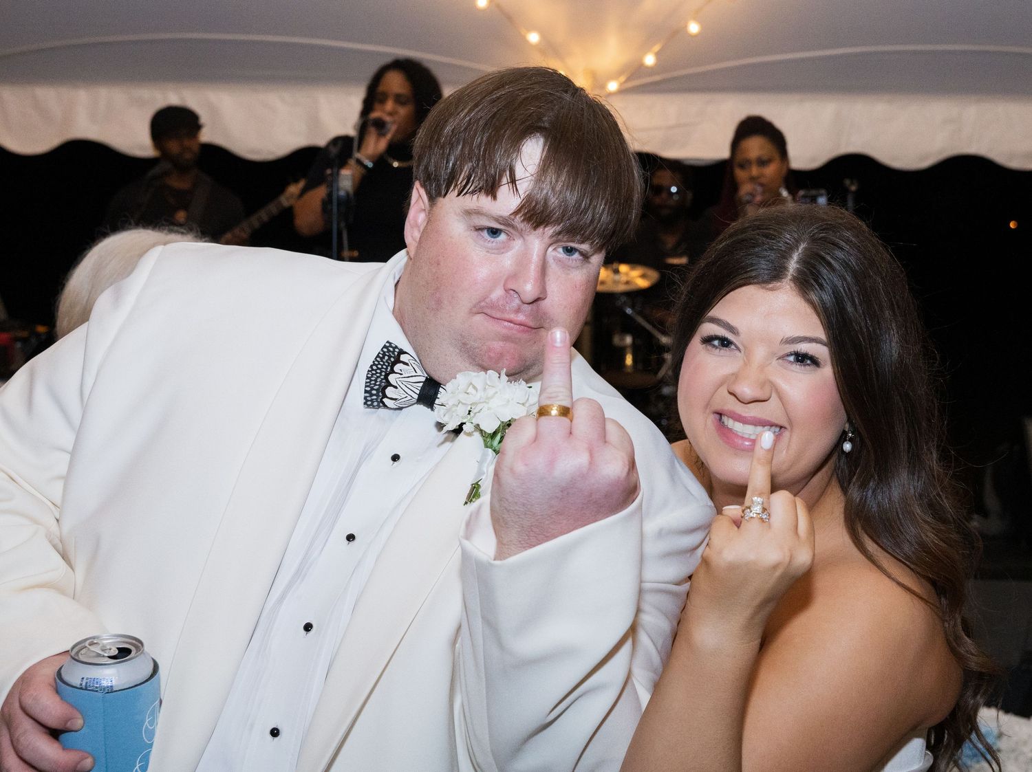 Bride and groom playfully show off wedding rings at lively tented wedding reception.