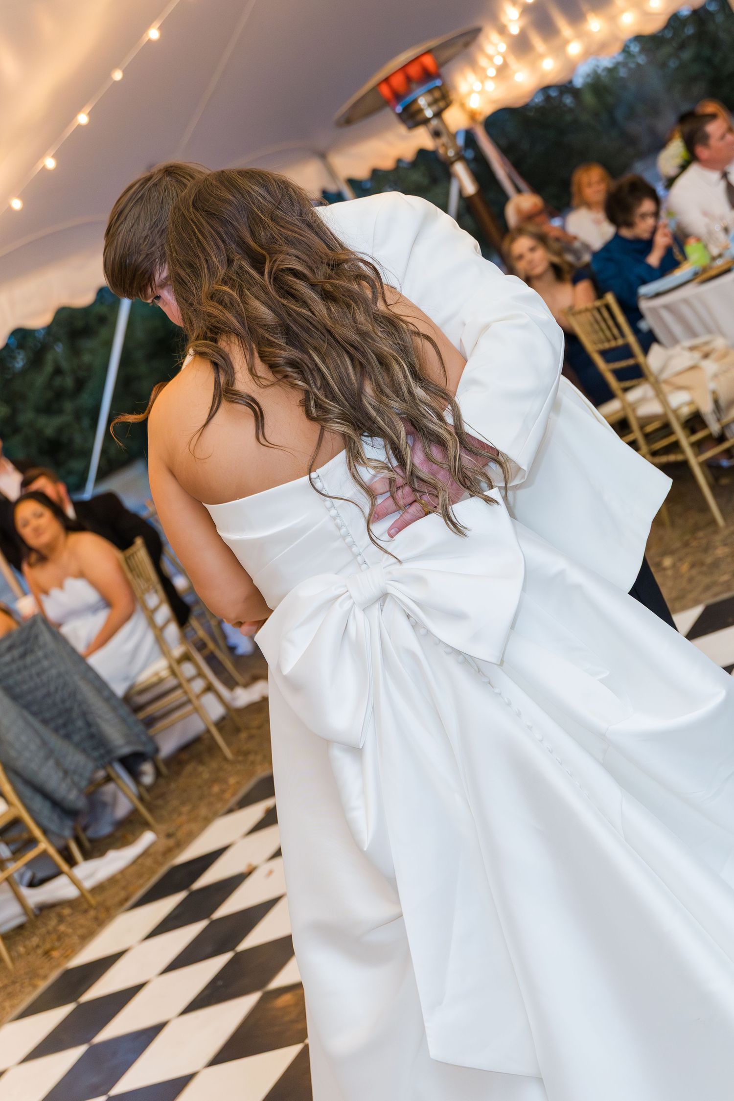 Bride and groom share first dance under tented reception with string lights and checkered floor.