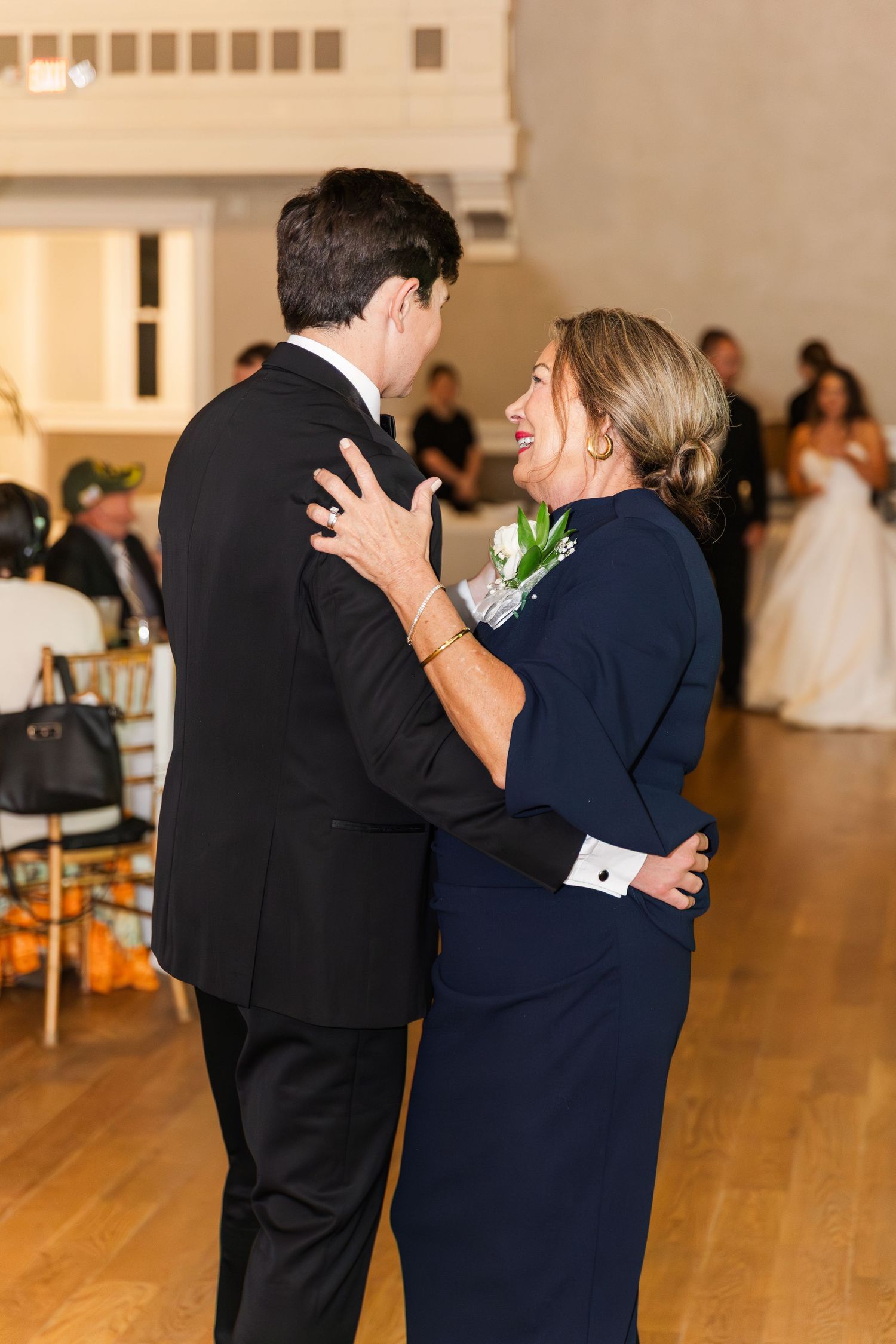 Groom shares a tender mother-son dance at wedding reception, both smiling warmly in elegant attire.