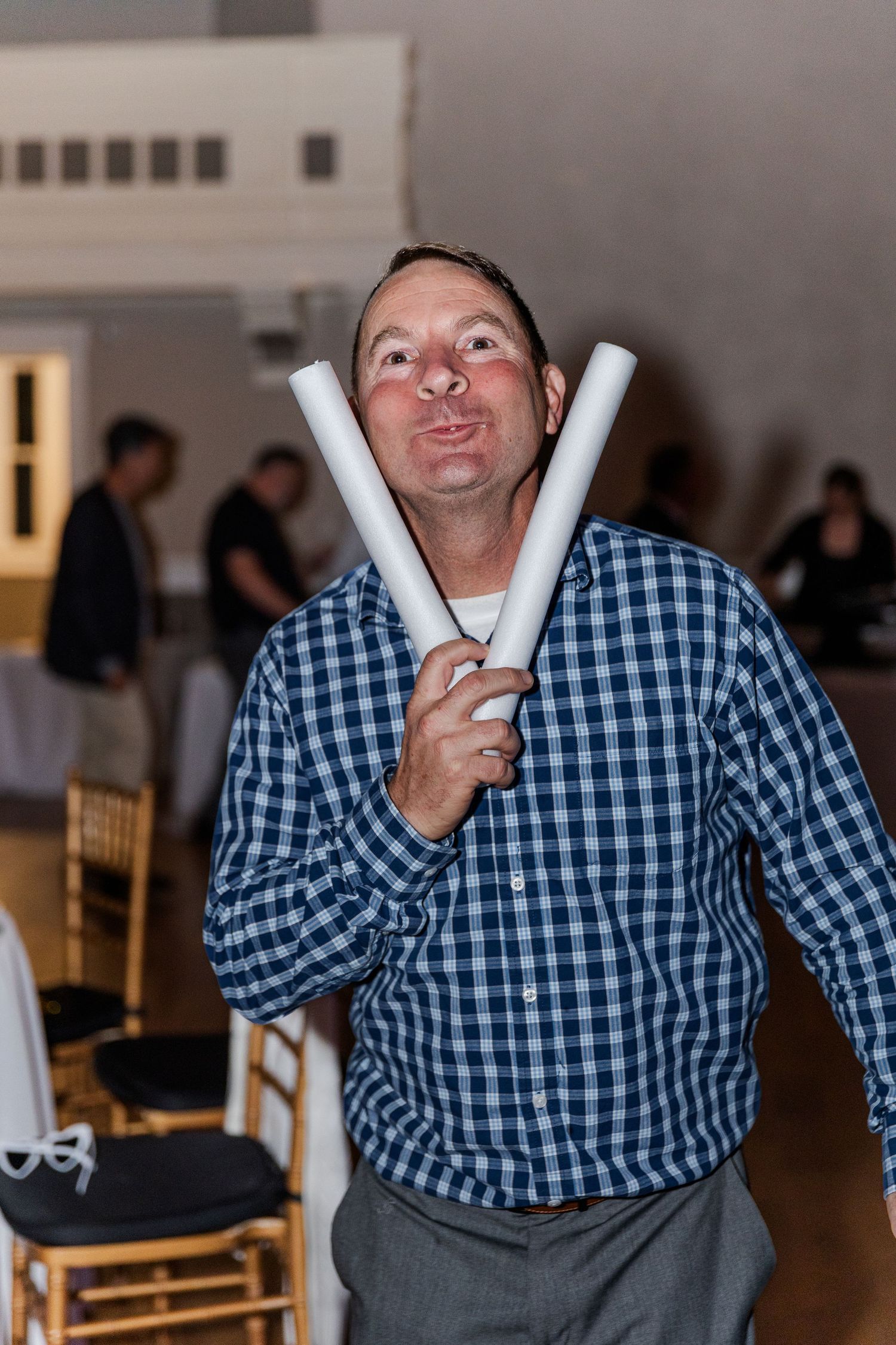 Man in plaid shirt humorously poses with two white glow sticks at a wedding reception.