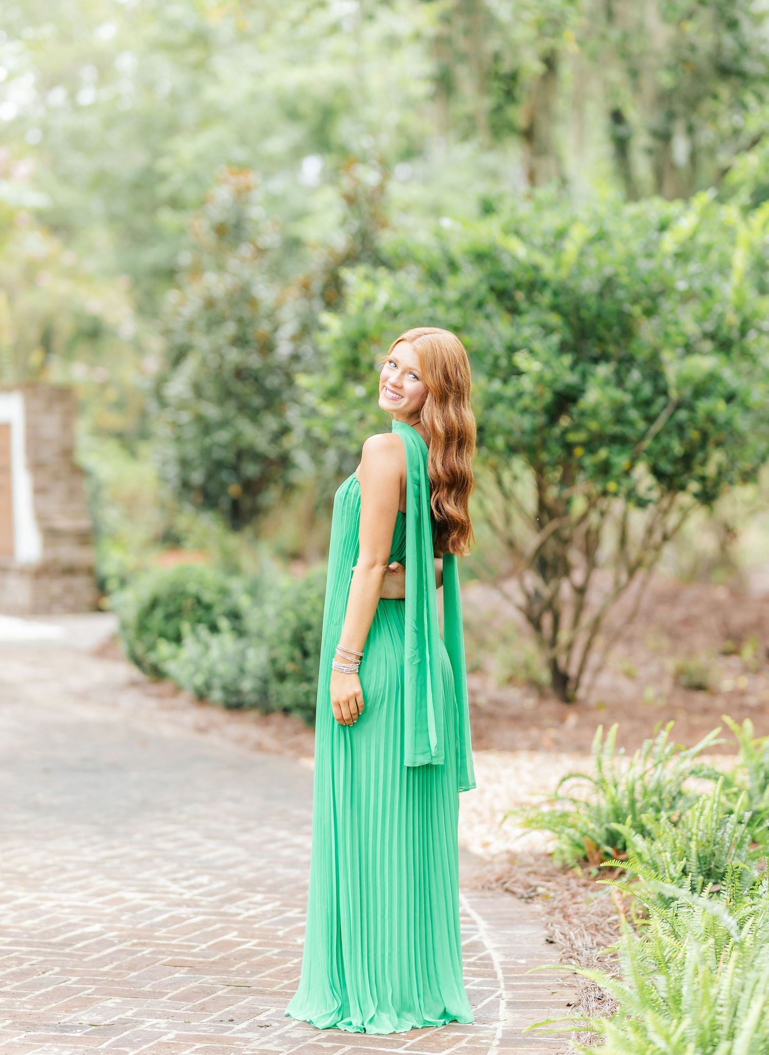 A woman in a flowing mint green maxi dress twirls gracefully in a garden setting with lush greenery in the background.