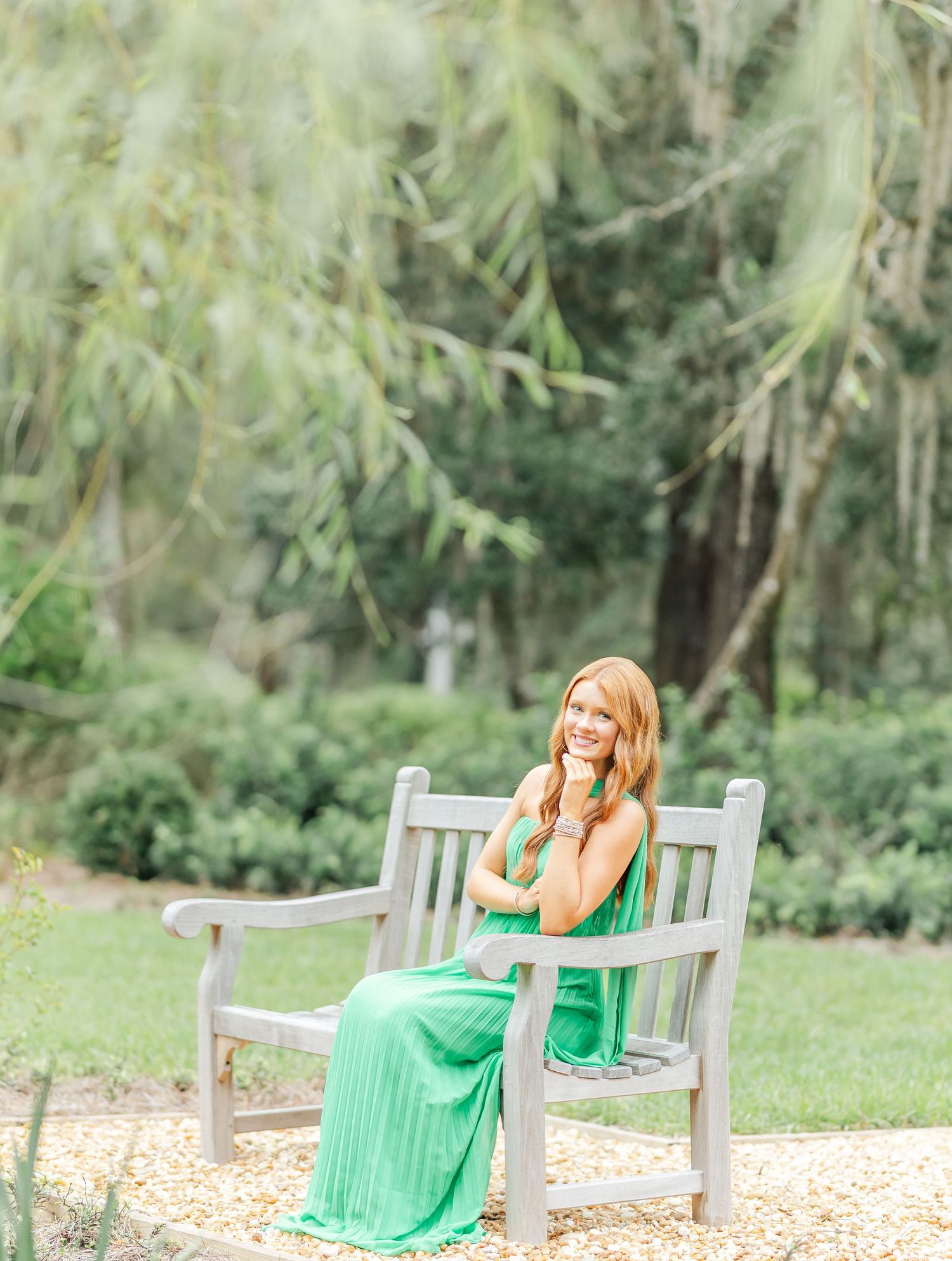 Outdoor photoshoot on a wooden bench featuring a flowing emerald green dress in a garden setting.