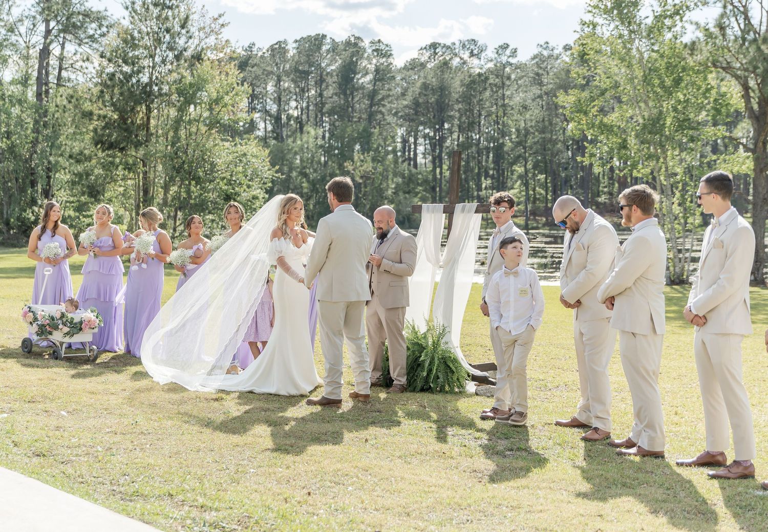Wedding party stands in formation during an outdoor ceremony with tall pine trees in the background.