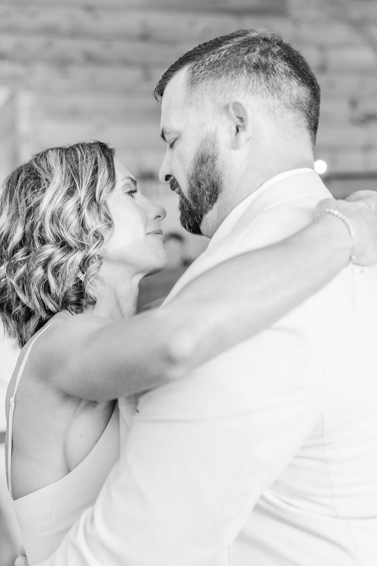Romantic black and white portrait of newlyweds sharing an intimate moment against a rustic wall backdrop.