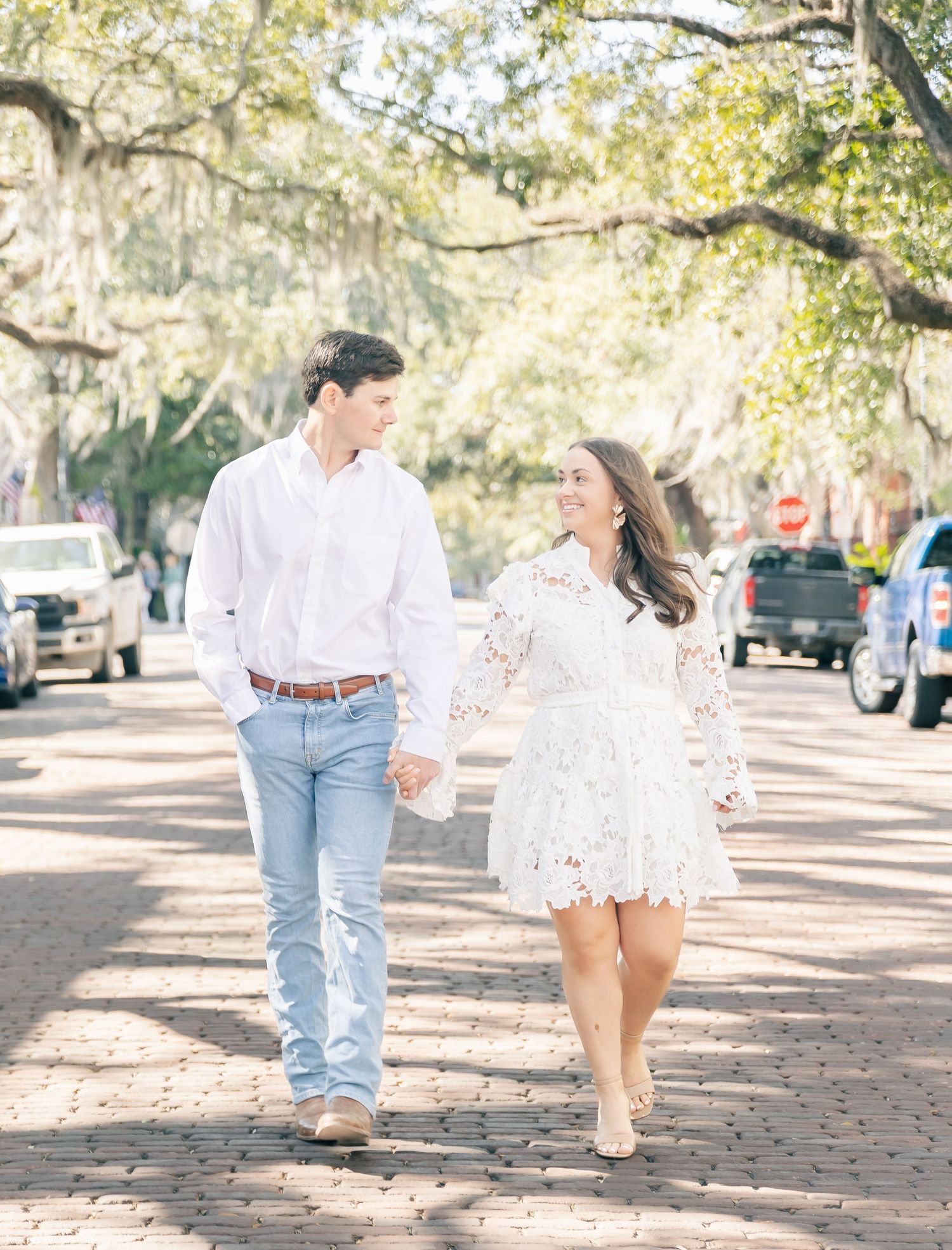 A couple takes a romantic walk down a tree-lined brick street.