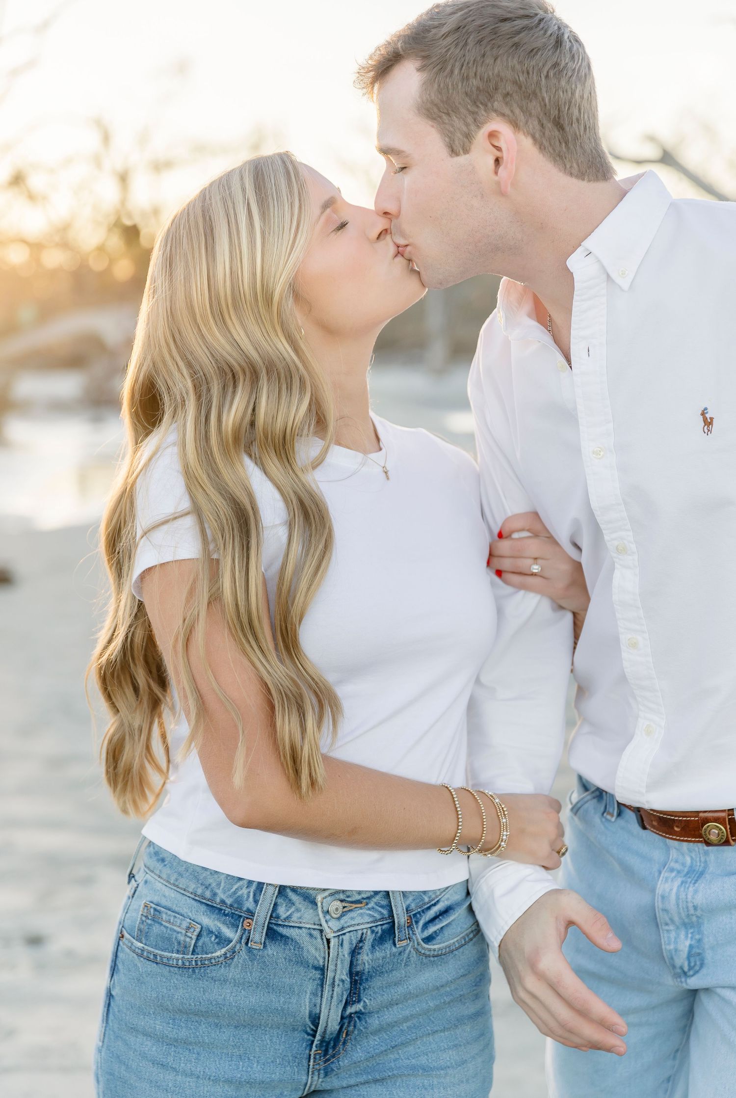 A romantic couple in white tops and jeans share an intimate kiss at sunset.