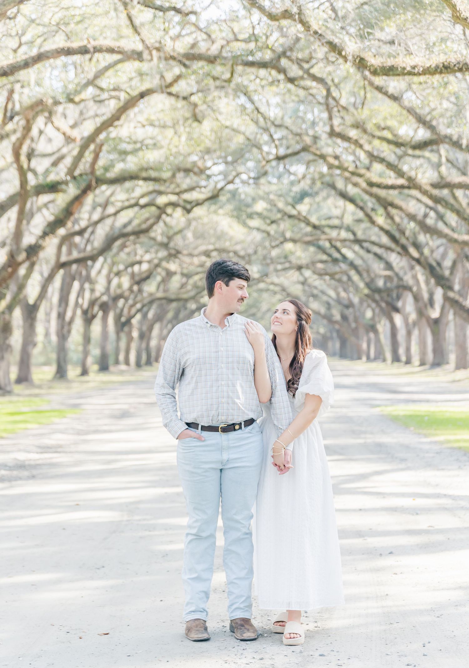 A couple shares a tender moment while standing on a tree-lined avenue in soft spring light.