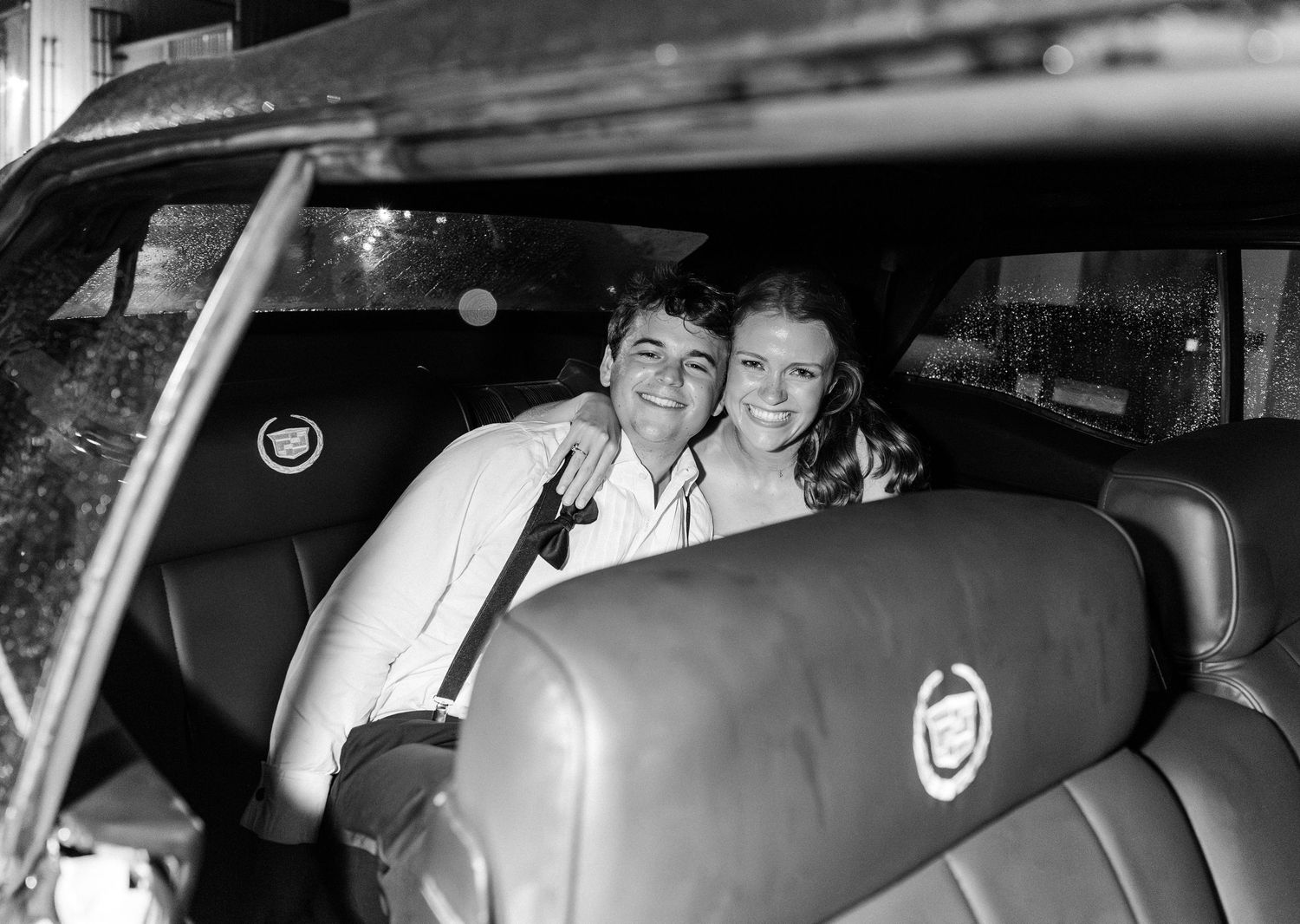 Happy newlyweds smile together in backseat of vintage Cadillac convertible after wedding.