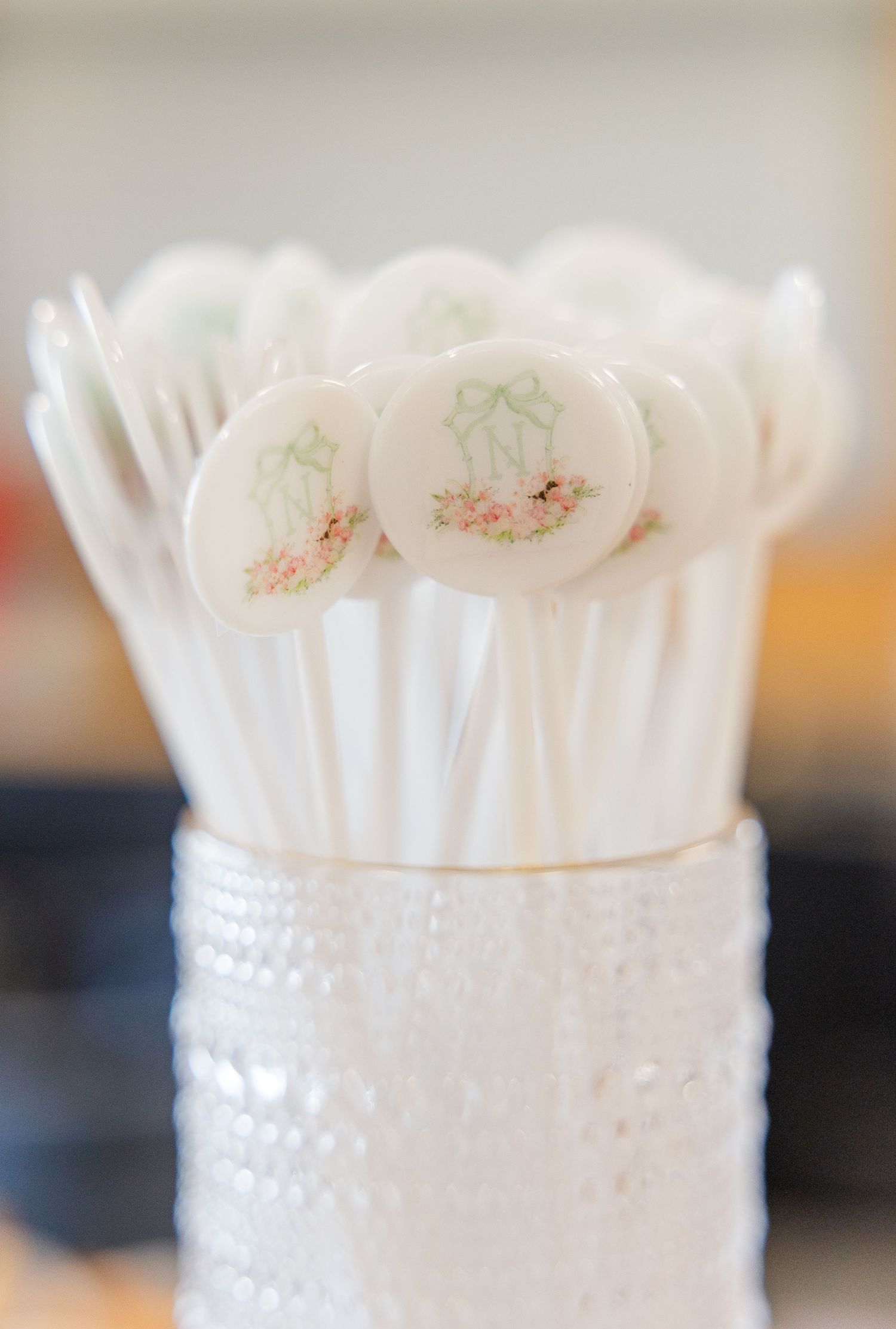 White wedding cake pops with delicate floral monogram designs displayed in a decorative white hobnail glass vase.