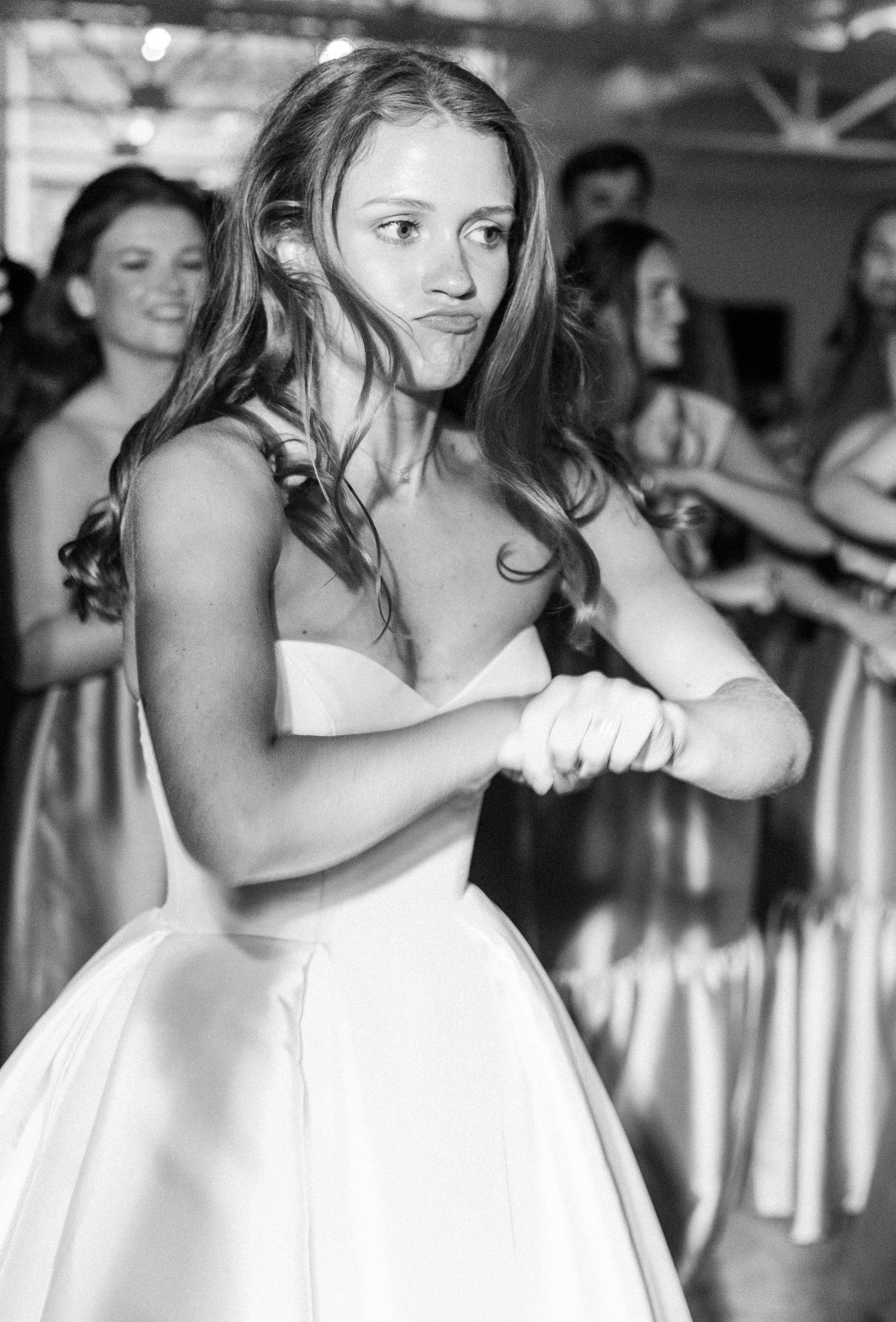 Black and white photo of bride dancing energetically in strapless ball gown at wedding reception.