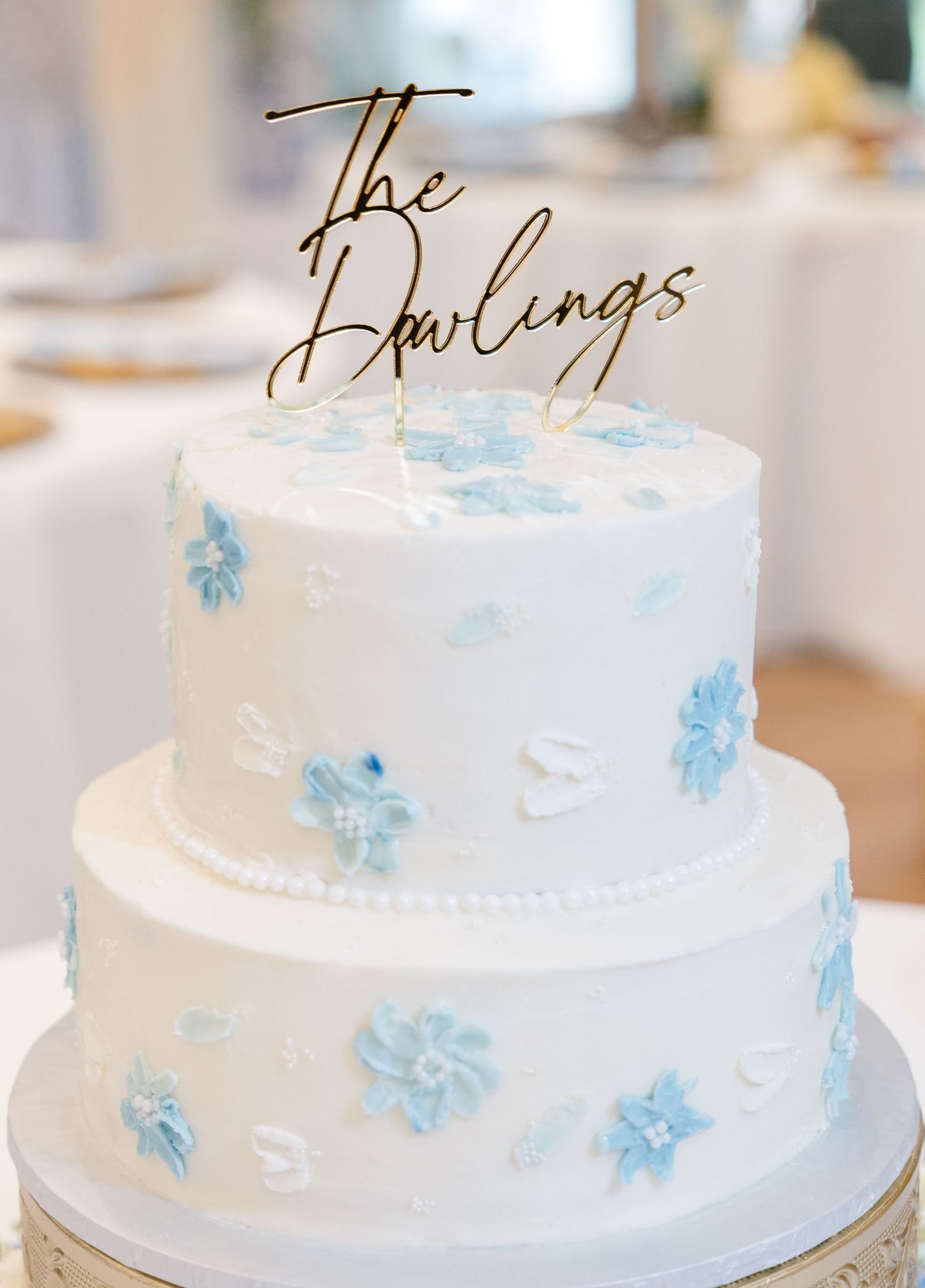 Two-tier white wedding cake with blue floral details and gold \