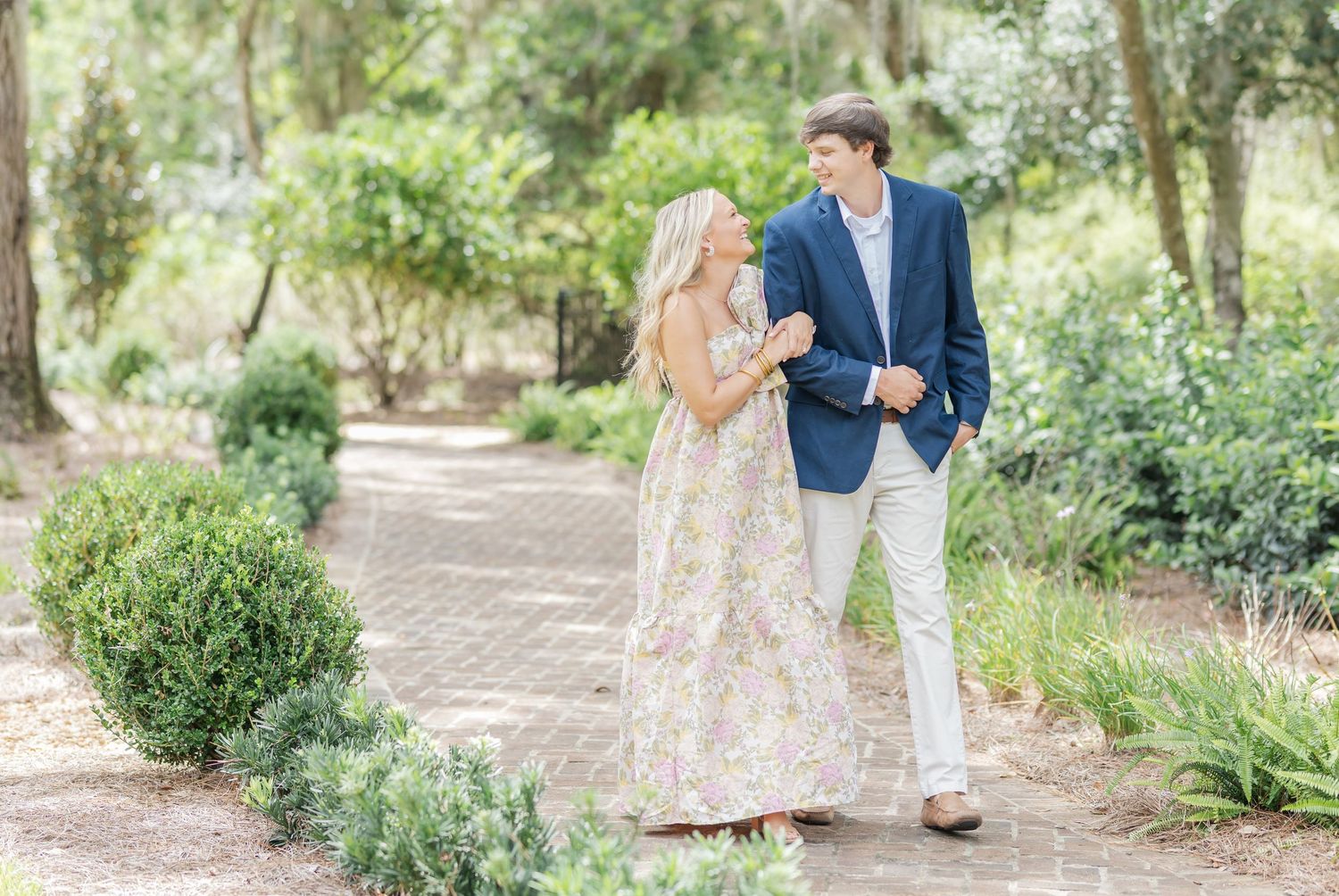 A couple takes romantic photos along a garden path surrounded by lush greenery.