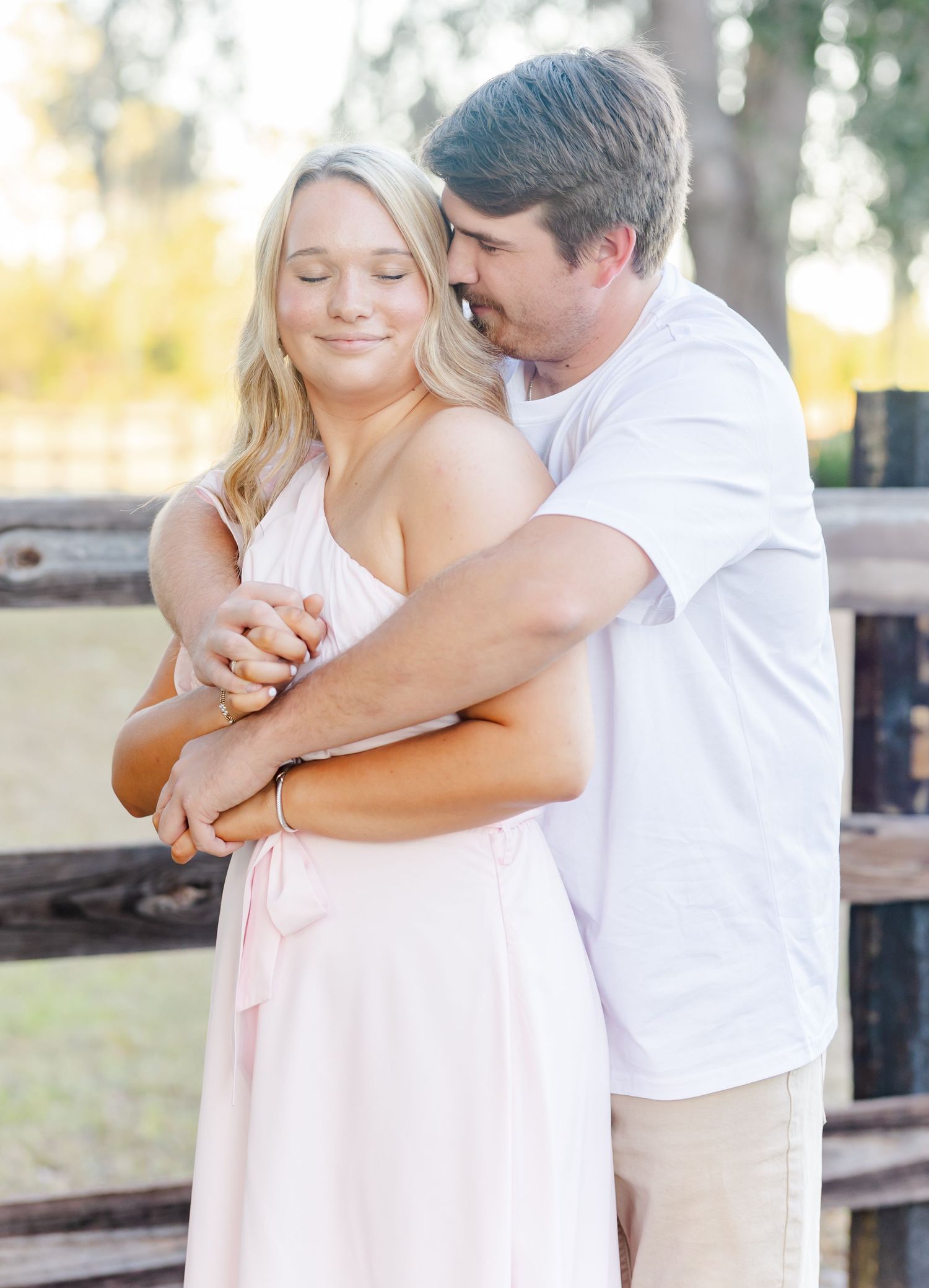 Romantic couple embraces near a rustic wooden fence during a golden hour photoshoot.