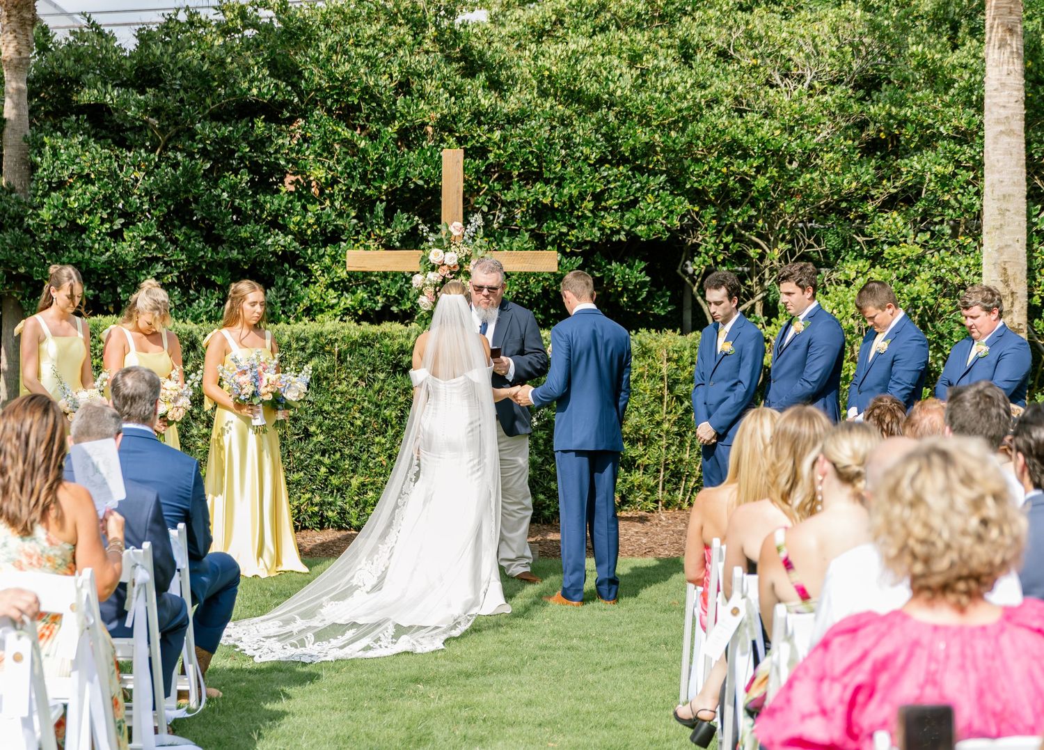 A panoramic view of an outdoor wedding ceremony on a lush green lawn with guests seated in white chairs.