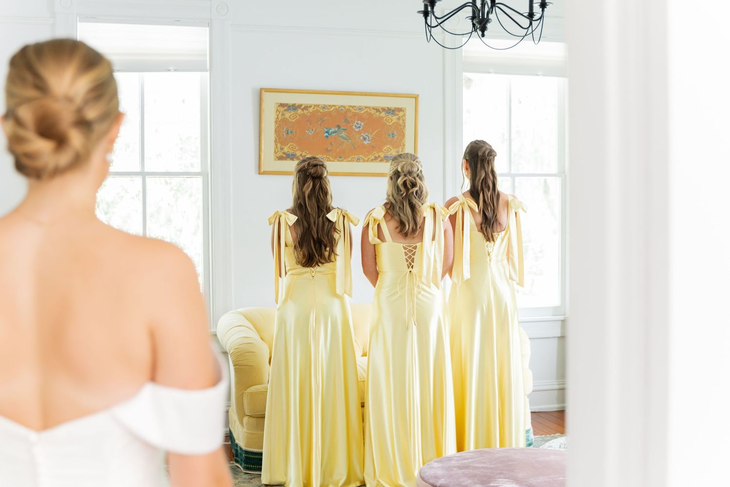 Bridesmaids in flowing yellow dresses stand in a row during a wedding preparation photoshoot.