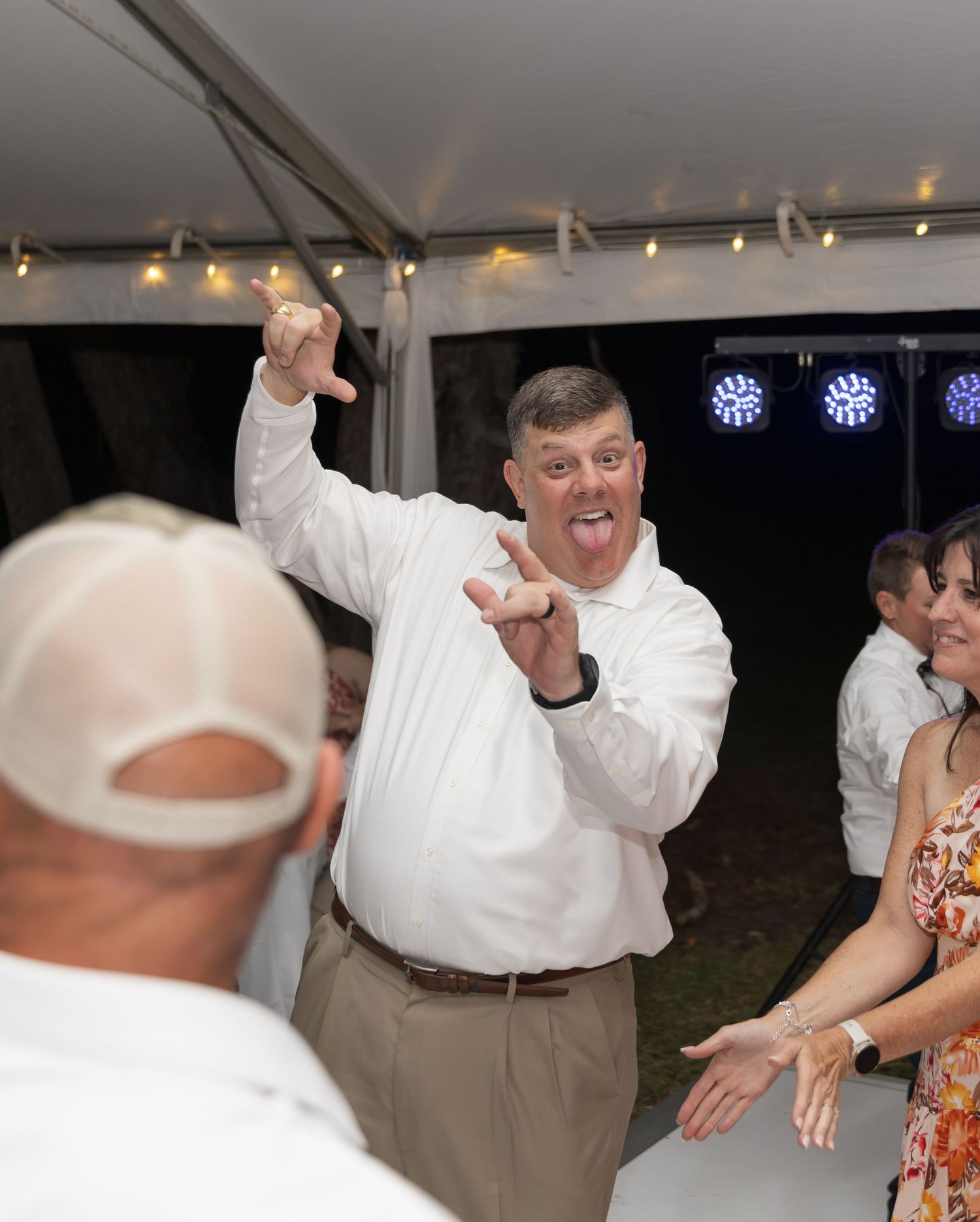 Guests dancing and celebrating at a wedding reception under a white tent with string lights.