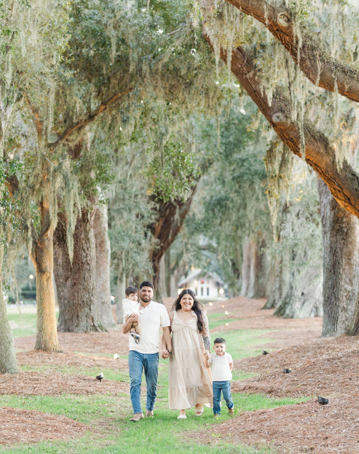 A family walks together under a canopy of Spanish moss-covered oak trees in a scenic park setting.