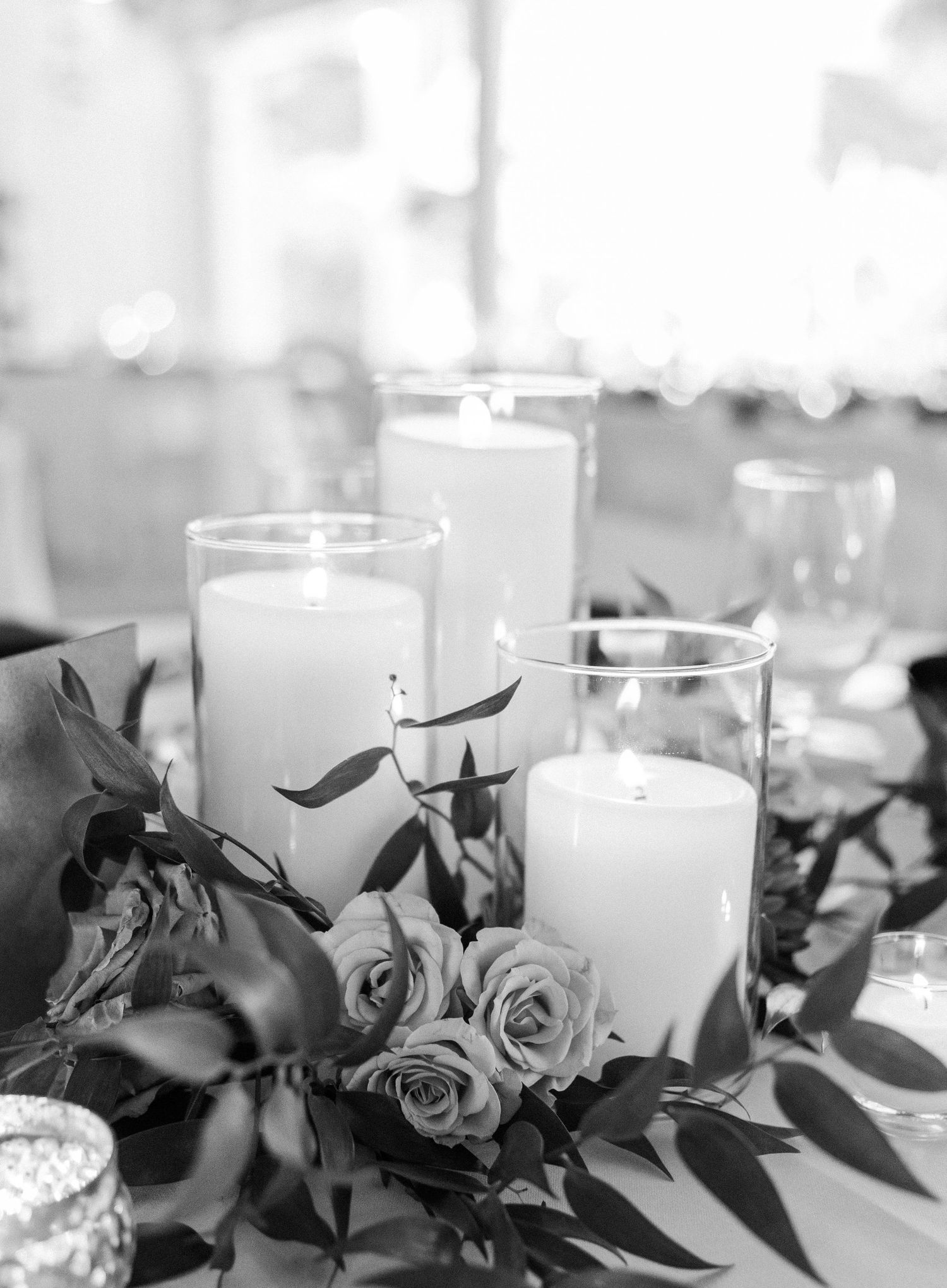 Black and white table decor featuring glass candle holders and rose arrangements for an elegant reception.