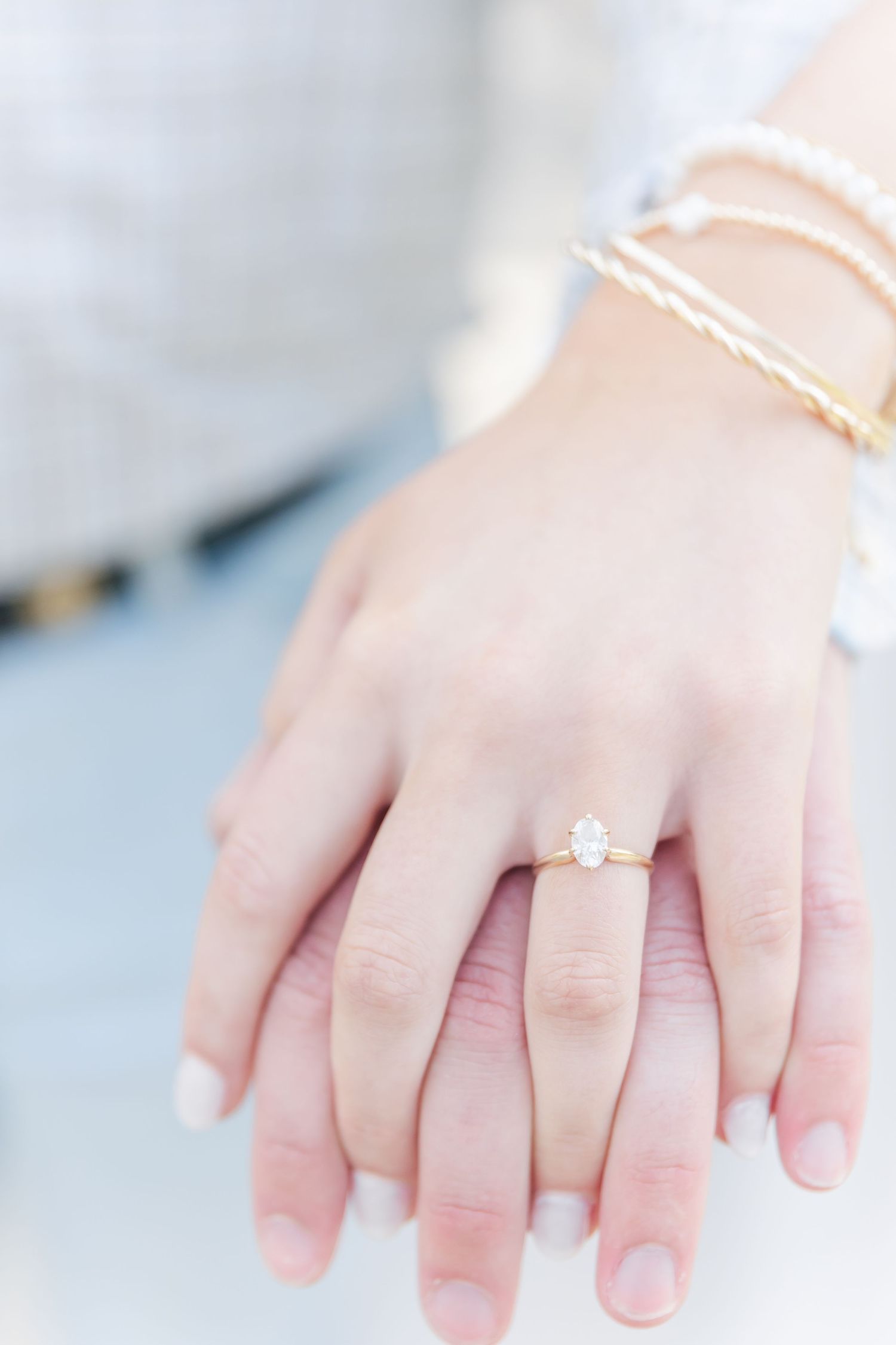 Close-up of a delicate engagement ring and stackable bracelets on a woman's hand.
