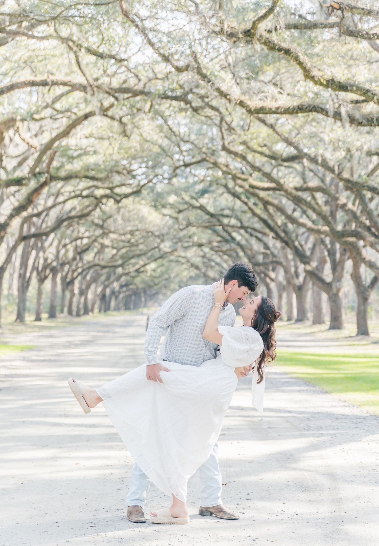 A couple shares a romantic dip pose under a canopy of oak trees.