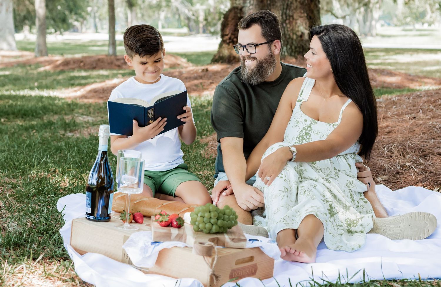 Family enjoying books and snacks during sunny afternoon picnic in park.