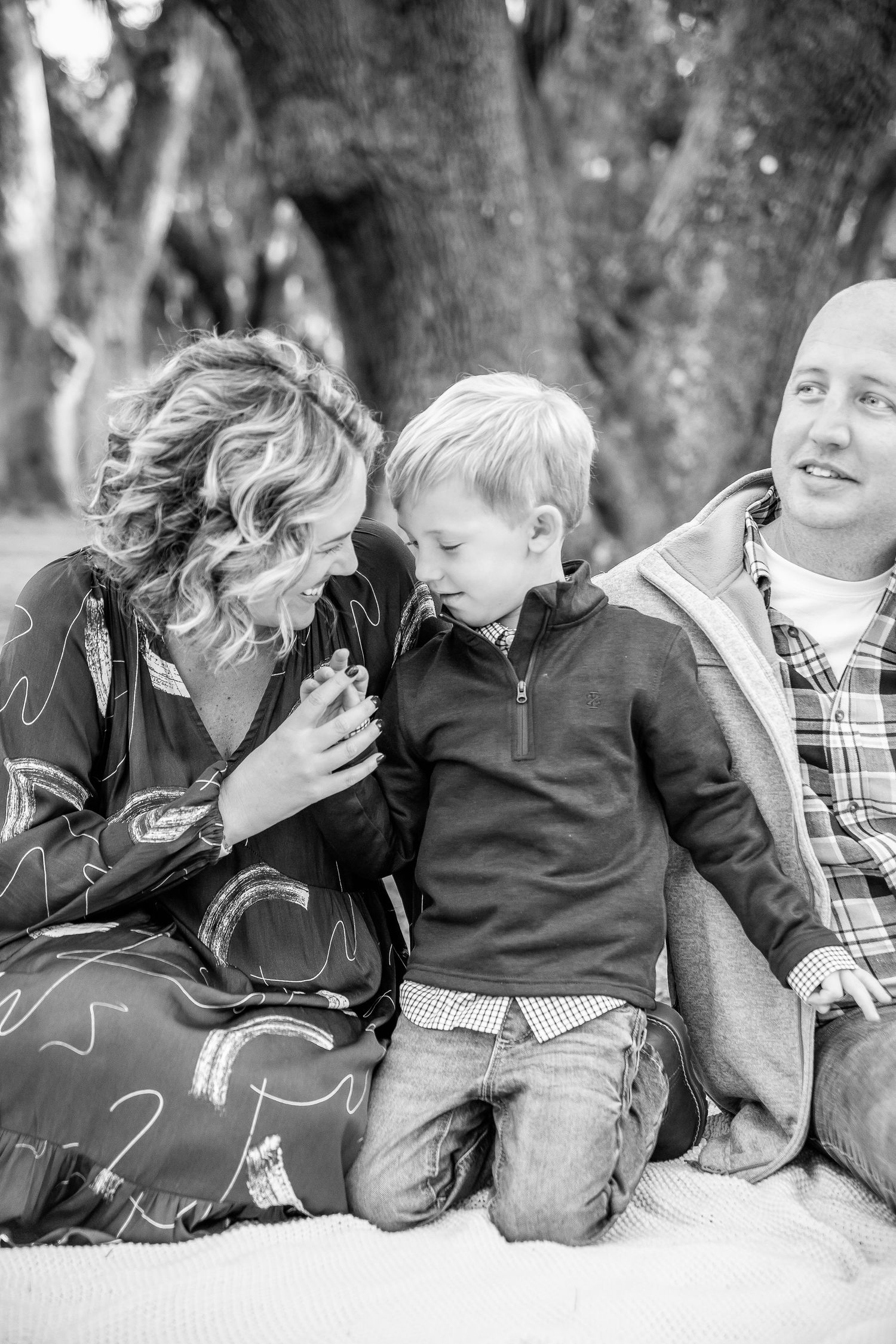 Black and white candid photo of family sharing intimate moment on blanket outdoors.