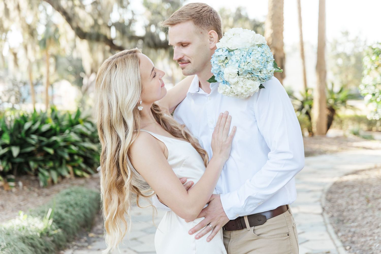 A tender romantic moment between a couple in white and khaki under Spanish moss trees.