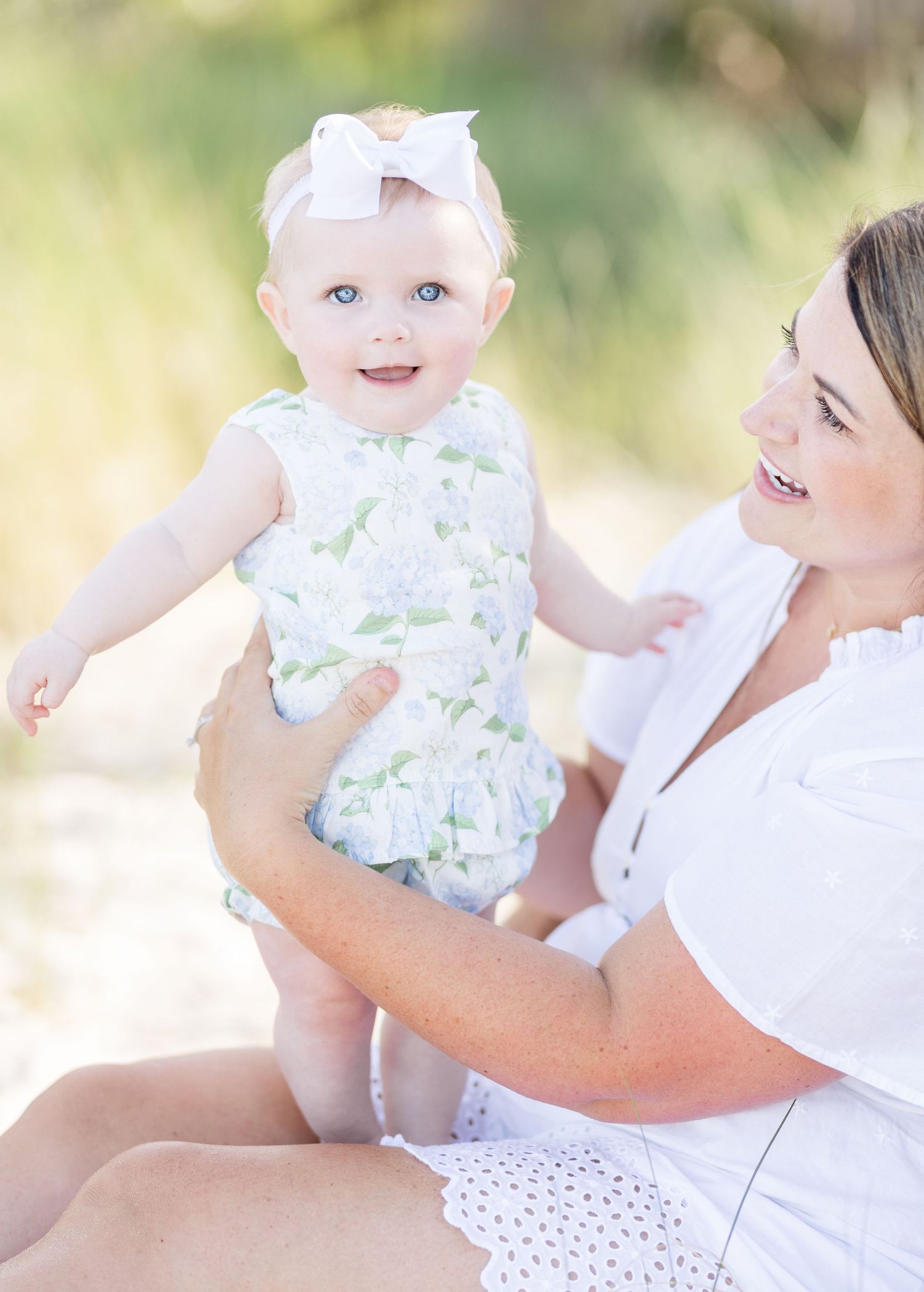 A heartwarming candid series shows a parent and baby in white outfits sharing joyful moments outdoors in natural light.