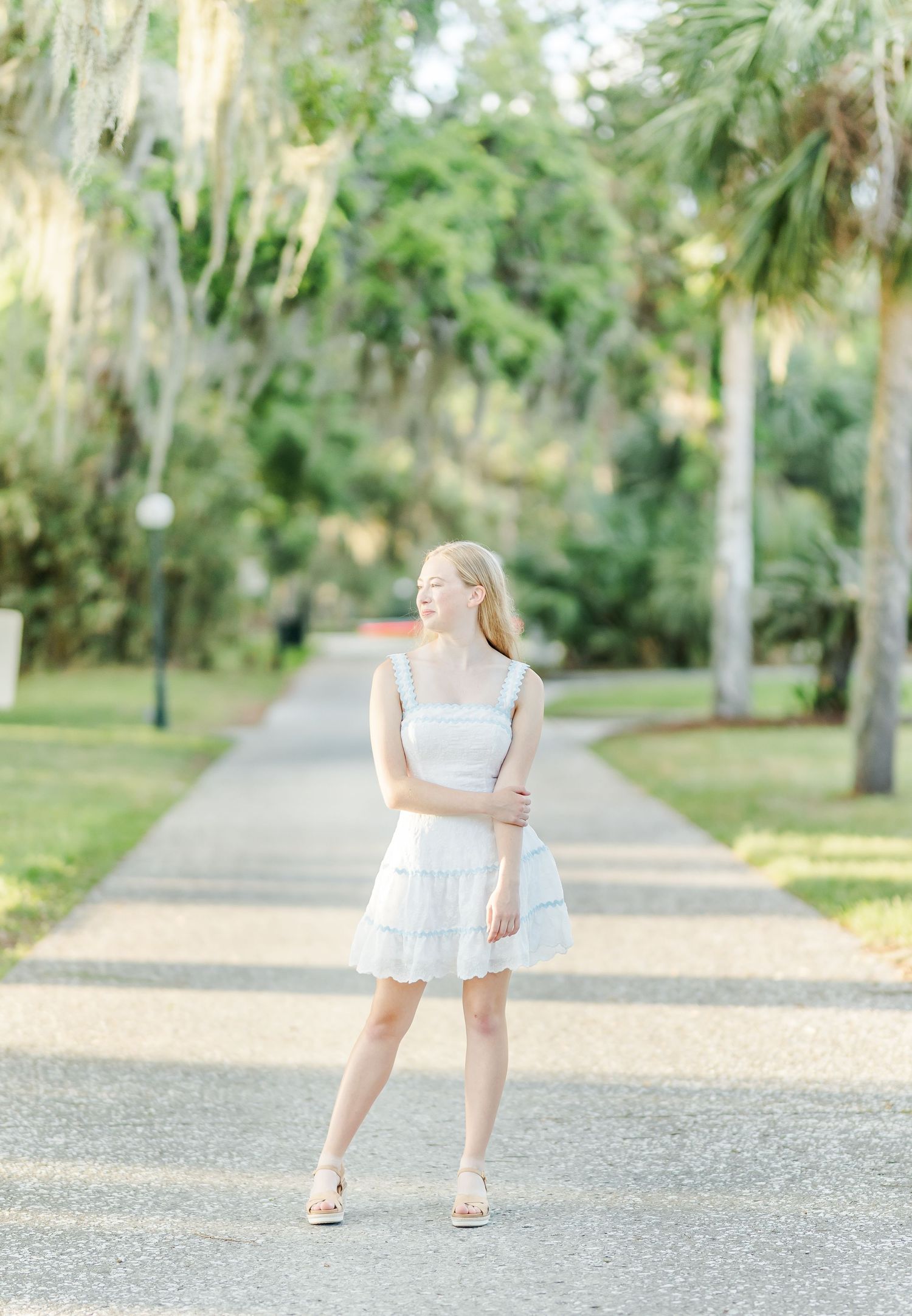 A series of five photos showing someone in a white dress walking along a gravel path in a lush green park setting.