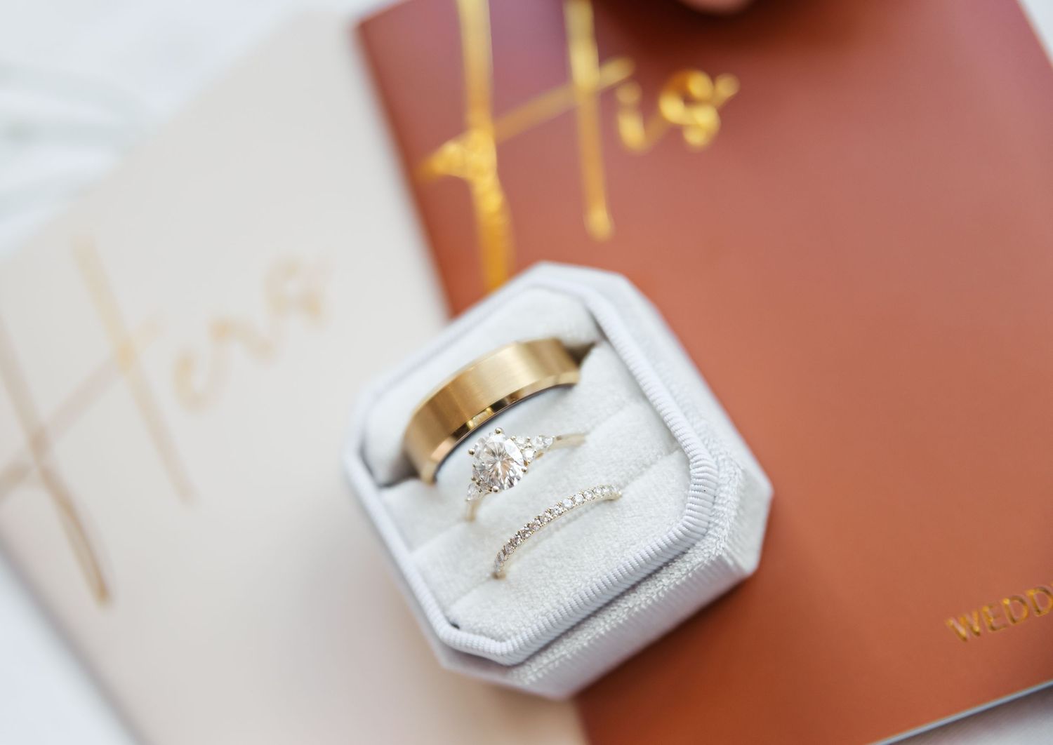 Wedding rings displayed in hexagonal white velvet ring box on burgundy surface.