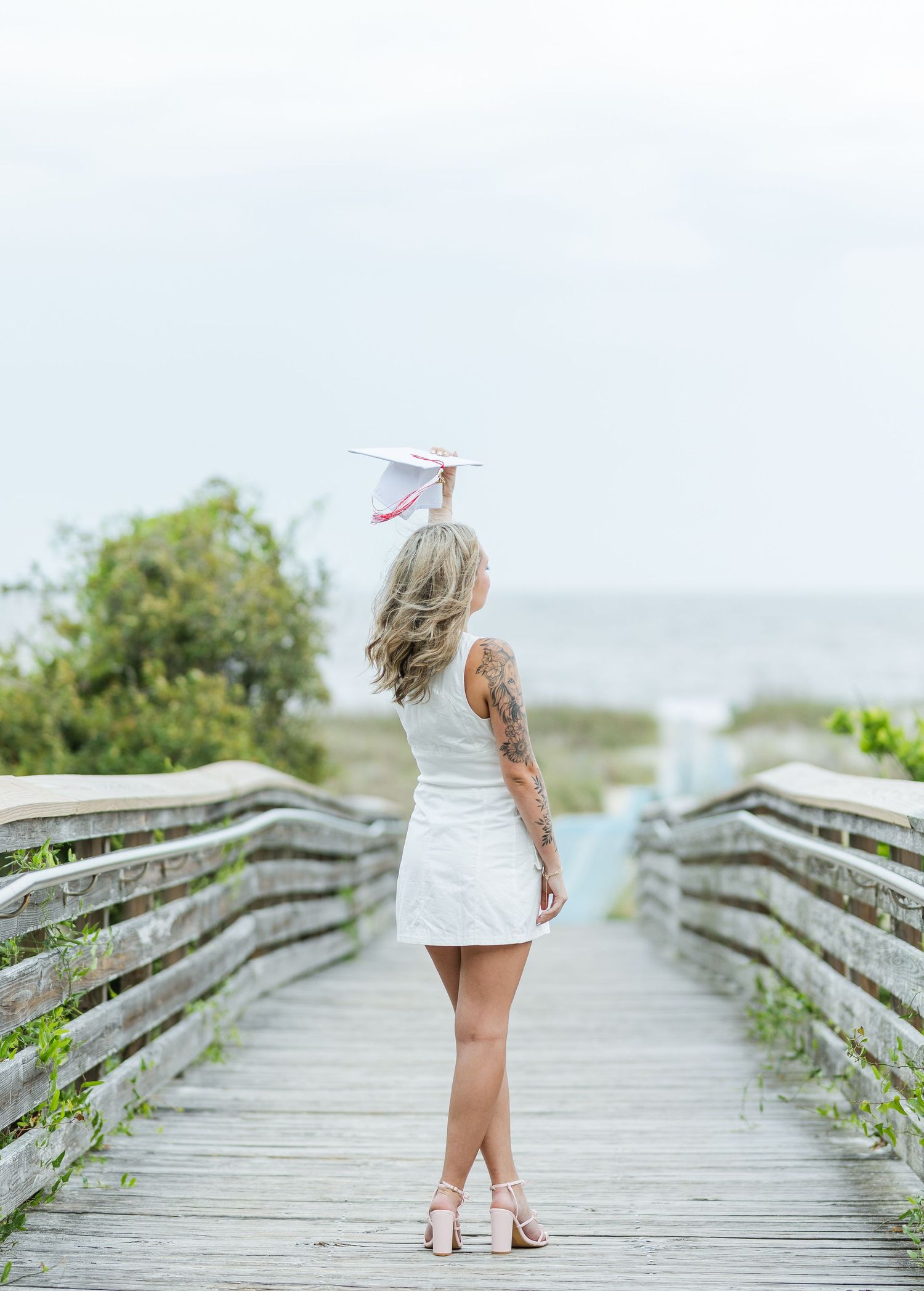 Graduate stands on wooden boardwalk overlooking coastal landscape.