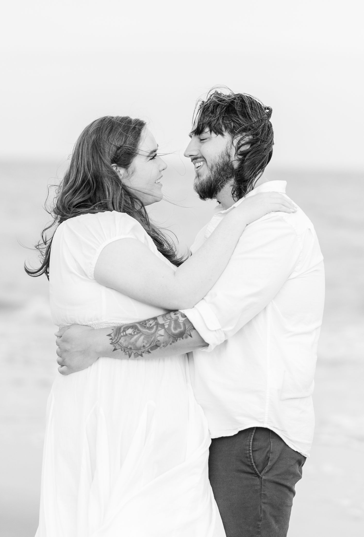 A couple shares an intimate moment in black and white photography by the ocean.