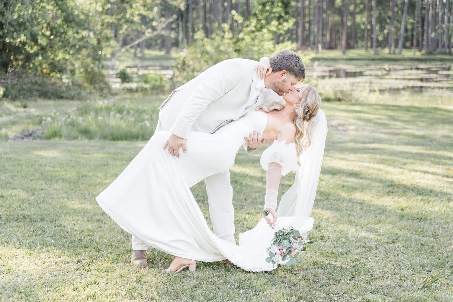 Romantic wedding couple in white sharing a dramatic dip kiss on their wedding day.