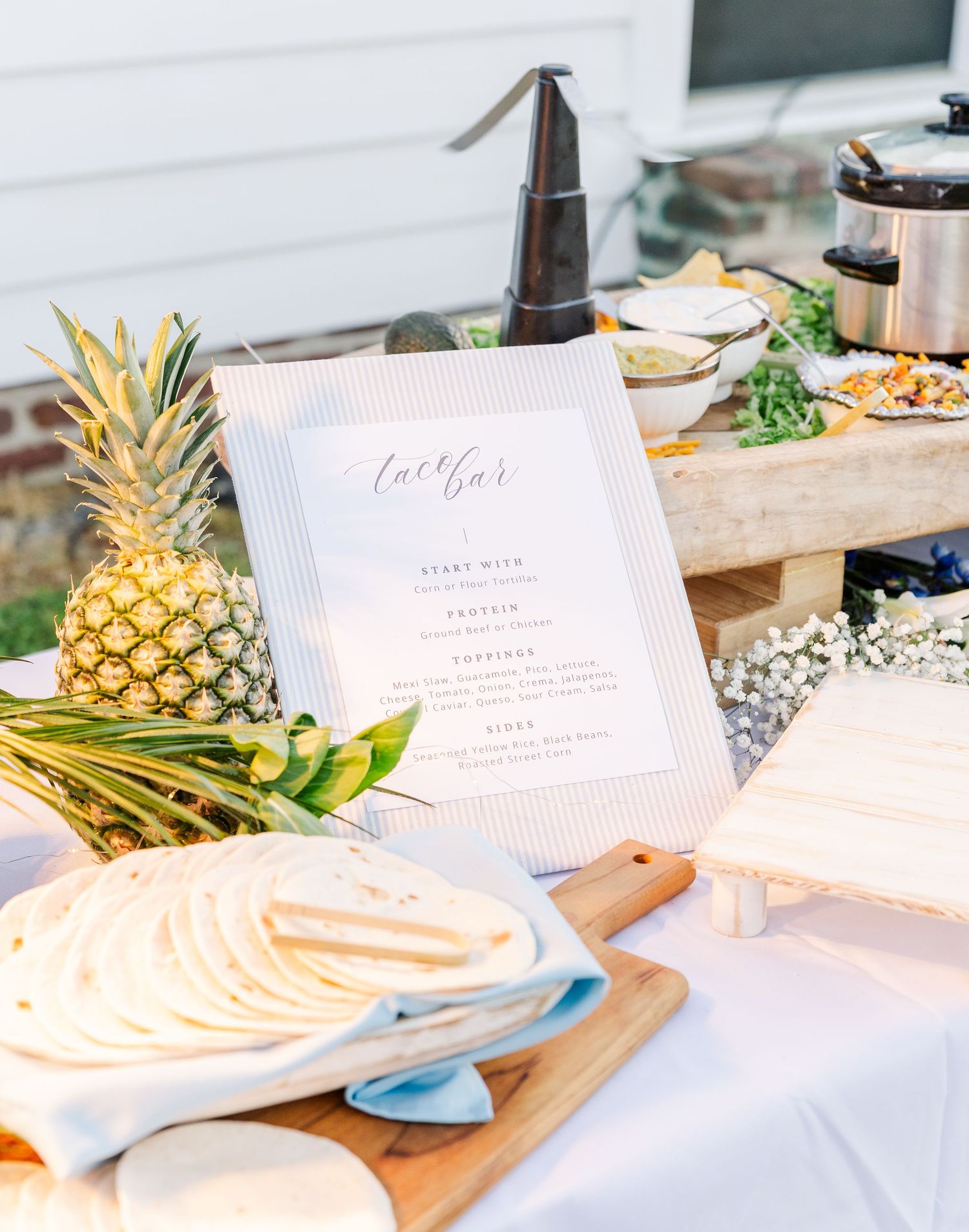Wedding taco bar display with tortillas, pineapple, and a decorative sign listing menu options.