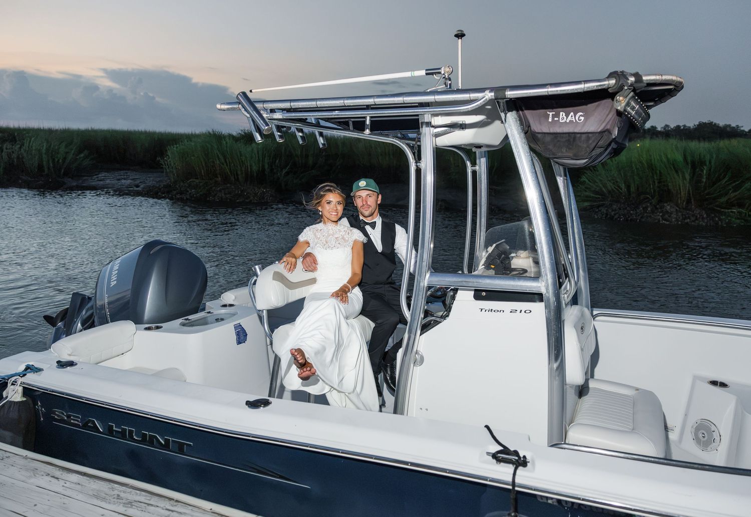 Bride and groom posing on a white center console boat near marshlands at dusk on their wedding day.
