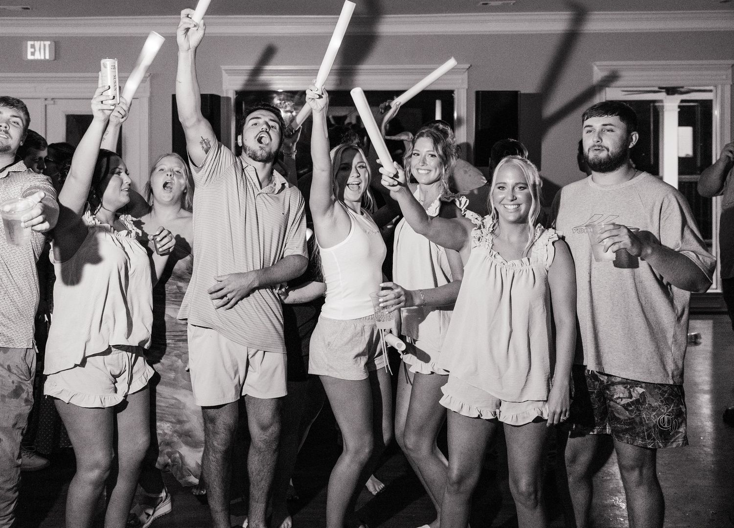 Black and white photo of wedding guests dancing and celebrating with glow sticks on the dance floor.