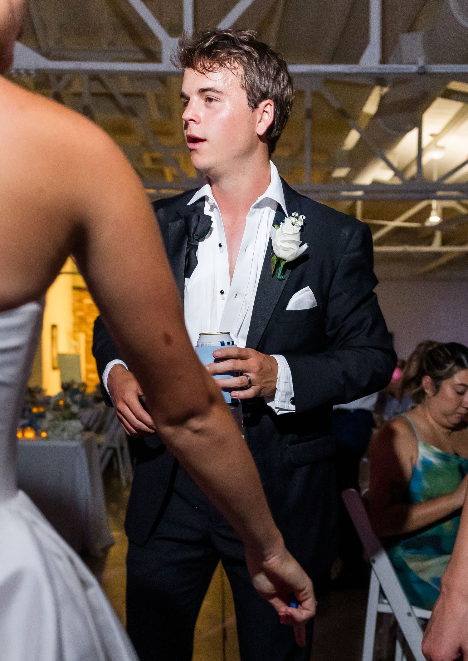 Young groomsman holding a drink socializes with bride at lively indoor wedding reception.