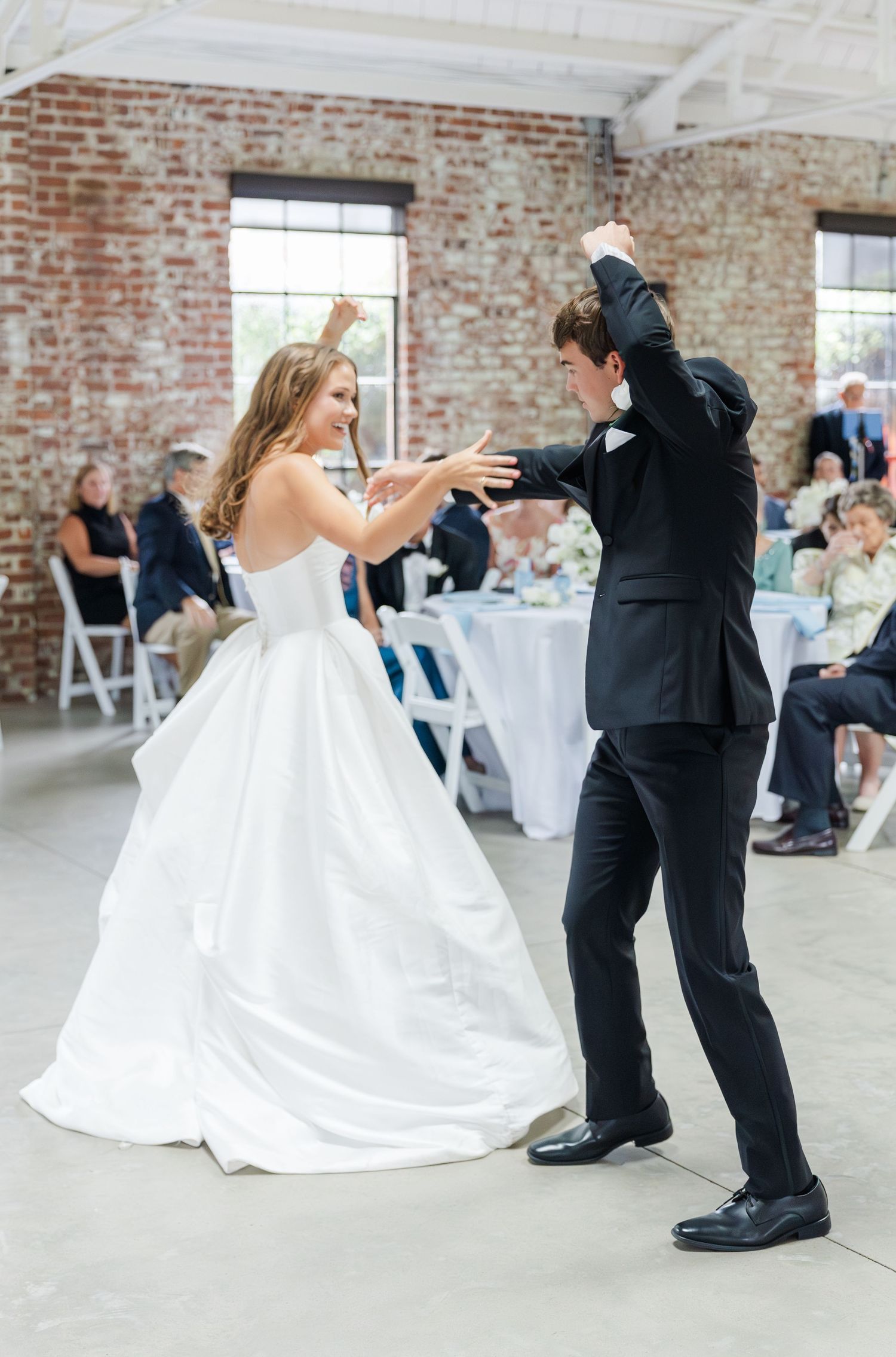 Bride and groom dancing joyfully at their wedding reception in a rustic brick venue.