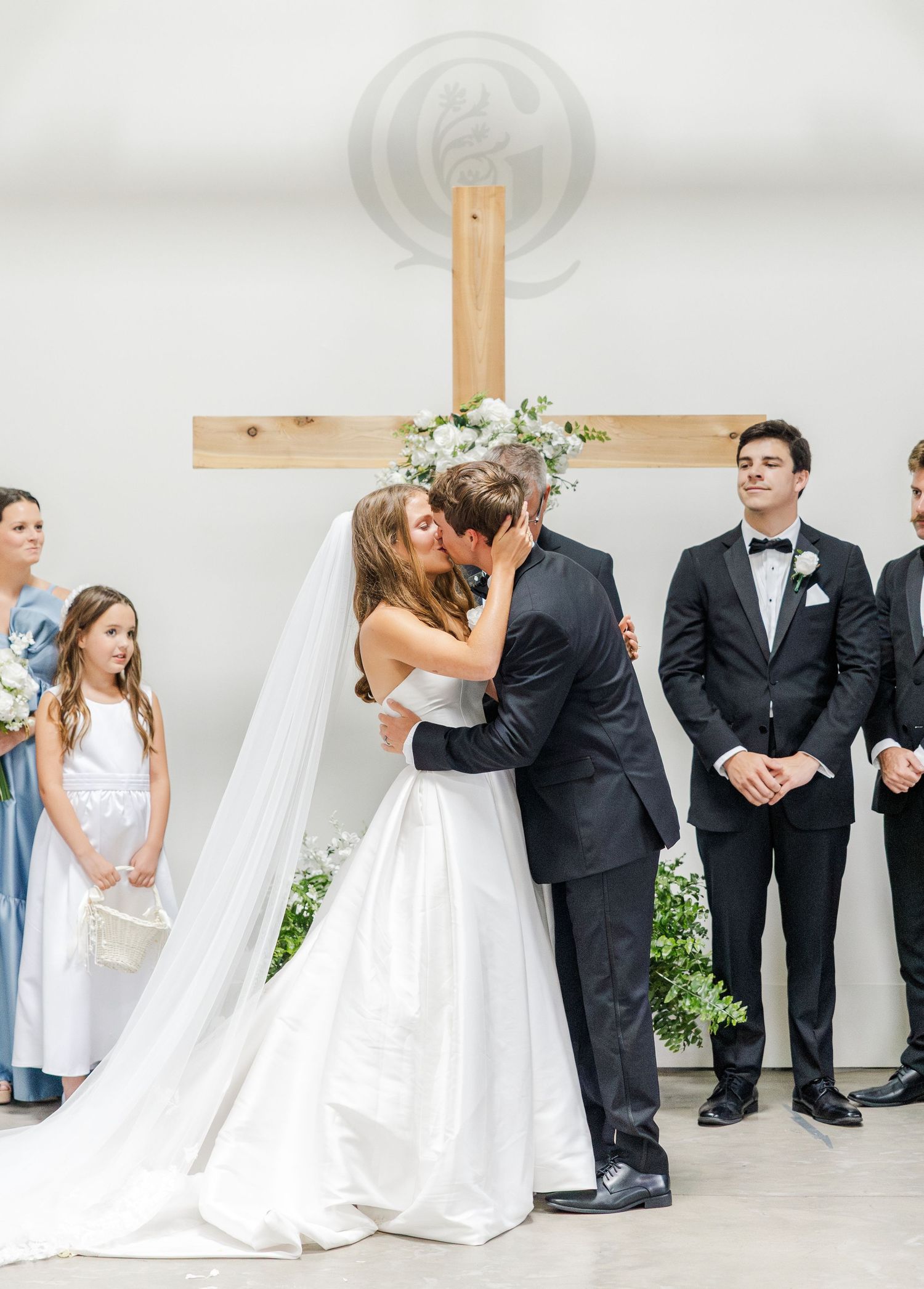 Bride and groom share their first kiss at the altar before a wooden cross.