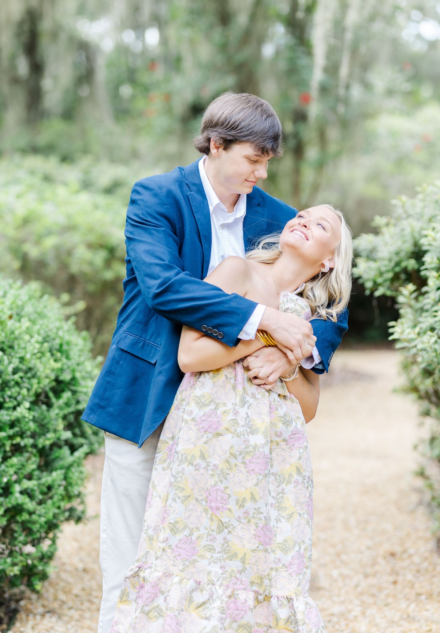 Playful couple in blue and floral outfits share romantic moments in a garden setting.