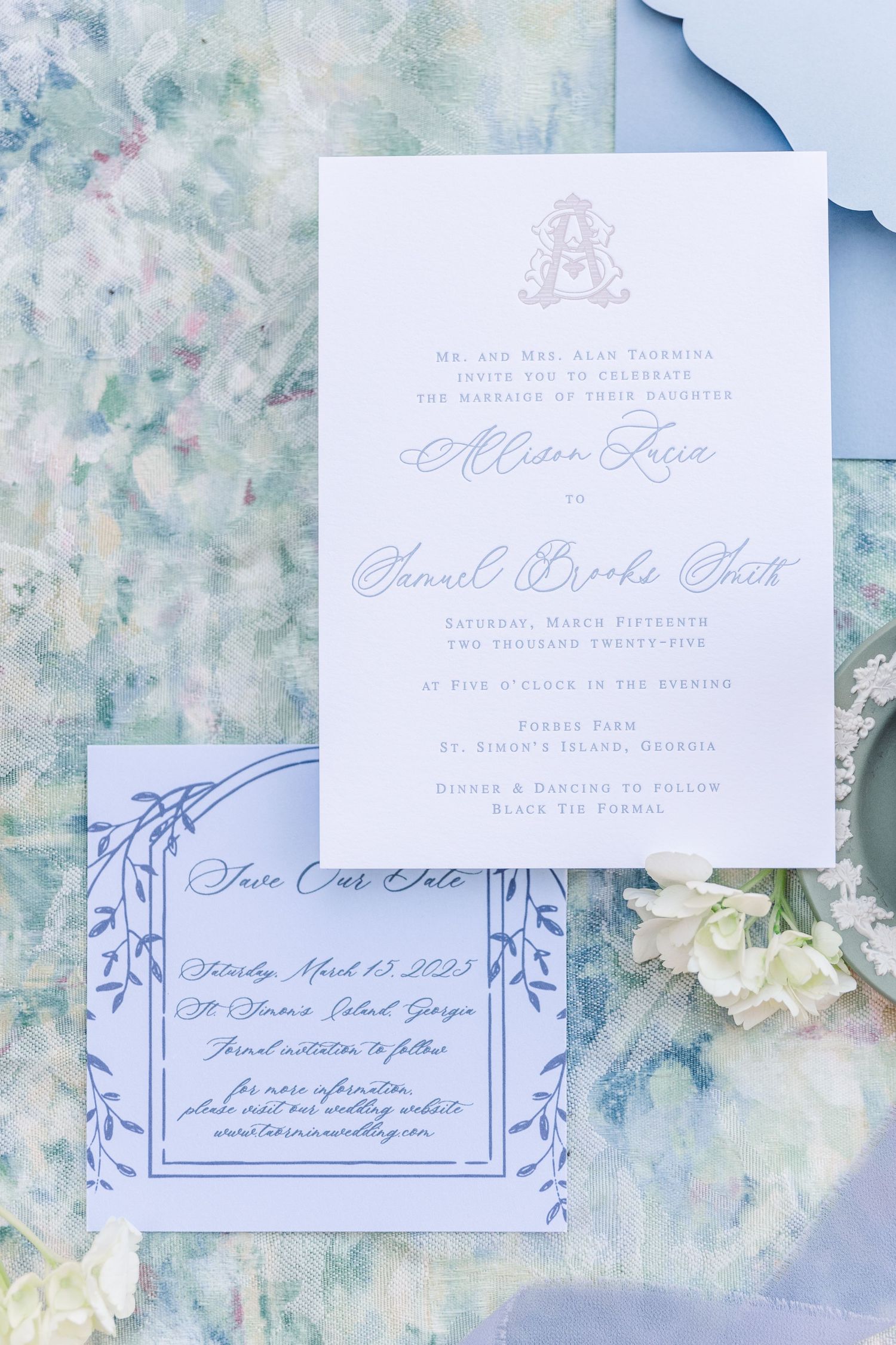 Elegant wedding invitation suite in light blue and white with delicate calligraphy and floral accents on marble background.