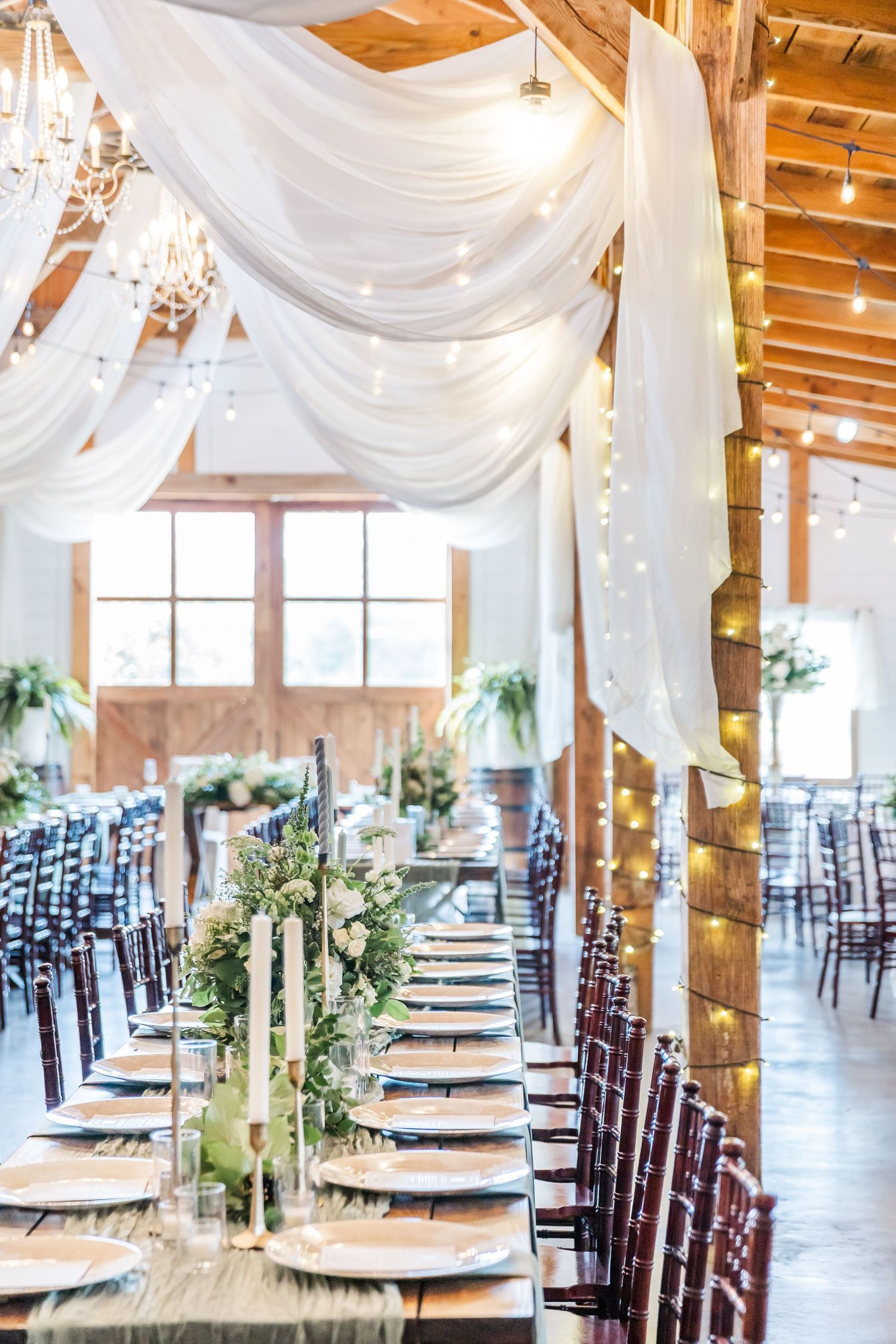 An elegant wedding reception venue with white draping, wooden beams, and mahogany chairs set for a celebration.