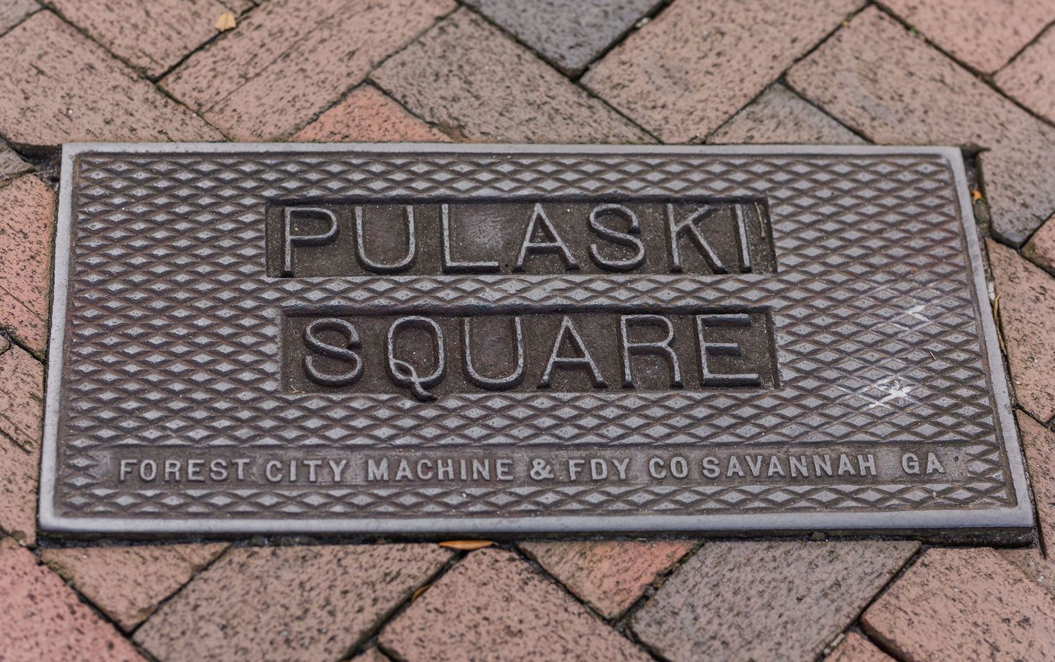 Metal plaque reading Pulaski Square embedded in brick pavement with geometric pattern.