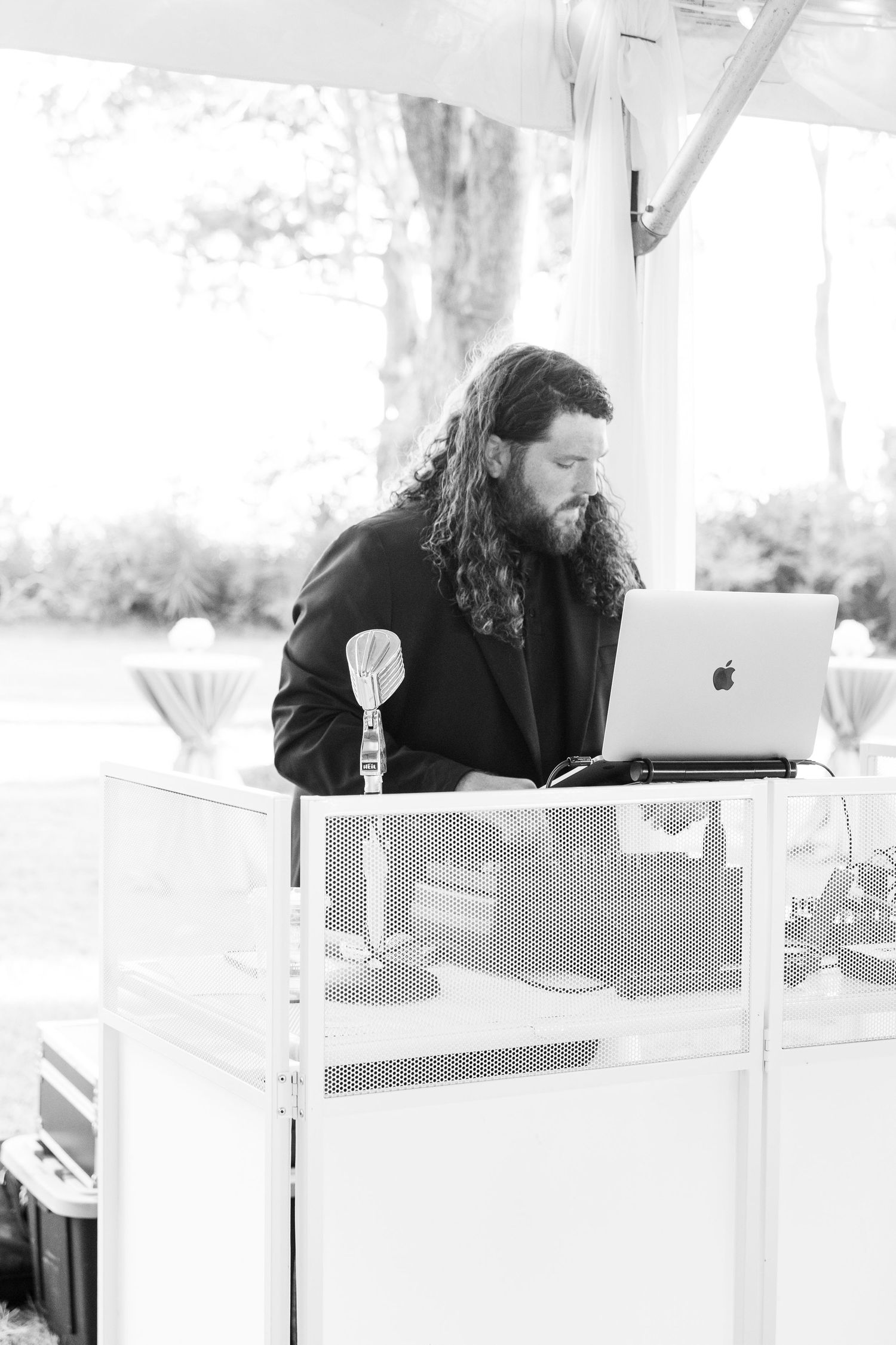 DJ working behind white booth equipment at an outdoor wedding reception.