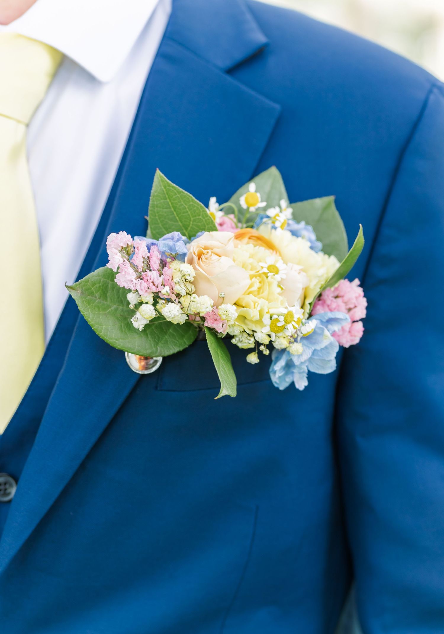 Delicate pink and white floral boutonnieres pinned to royal blue suit jackets in a wedding party lineup.