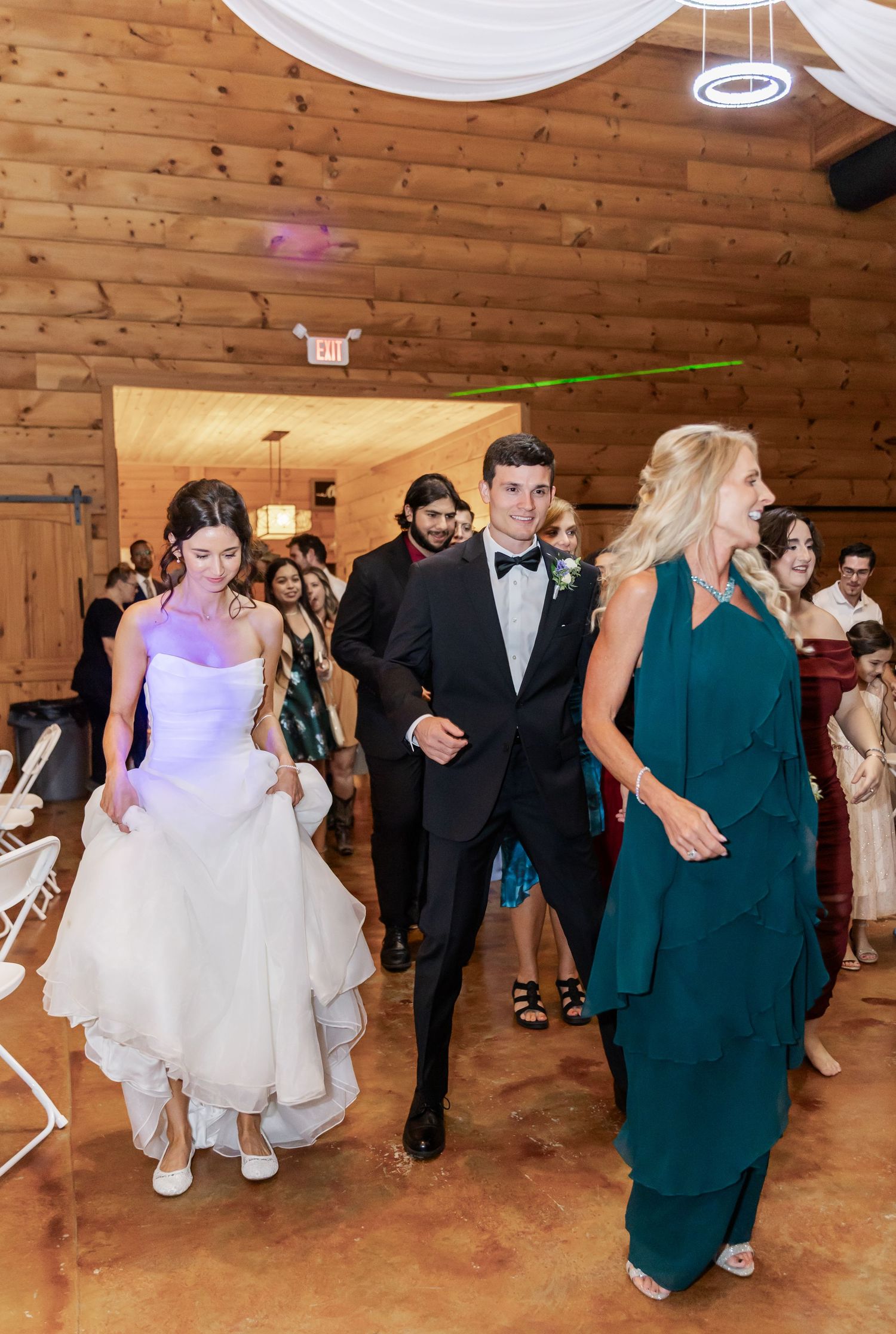 Wedding guests dancing and celebrating in a rustic wooden barn venue with decorative lighting.